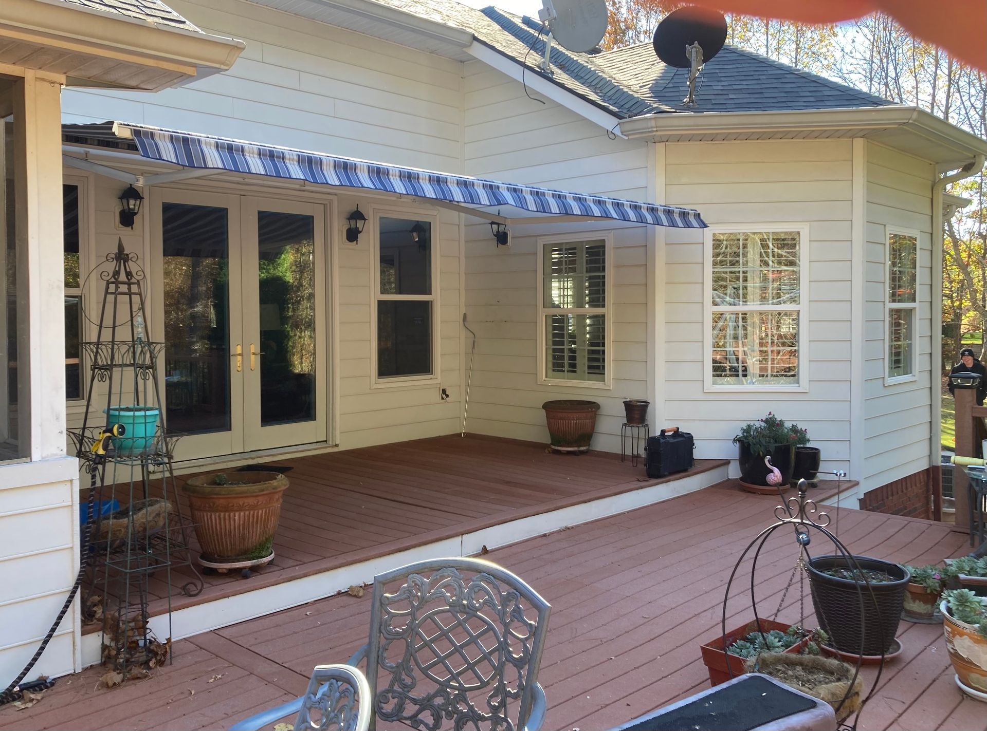 A deck with a striped awning, overlooking a backyard. House with white siding, french doors, and windows.