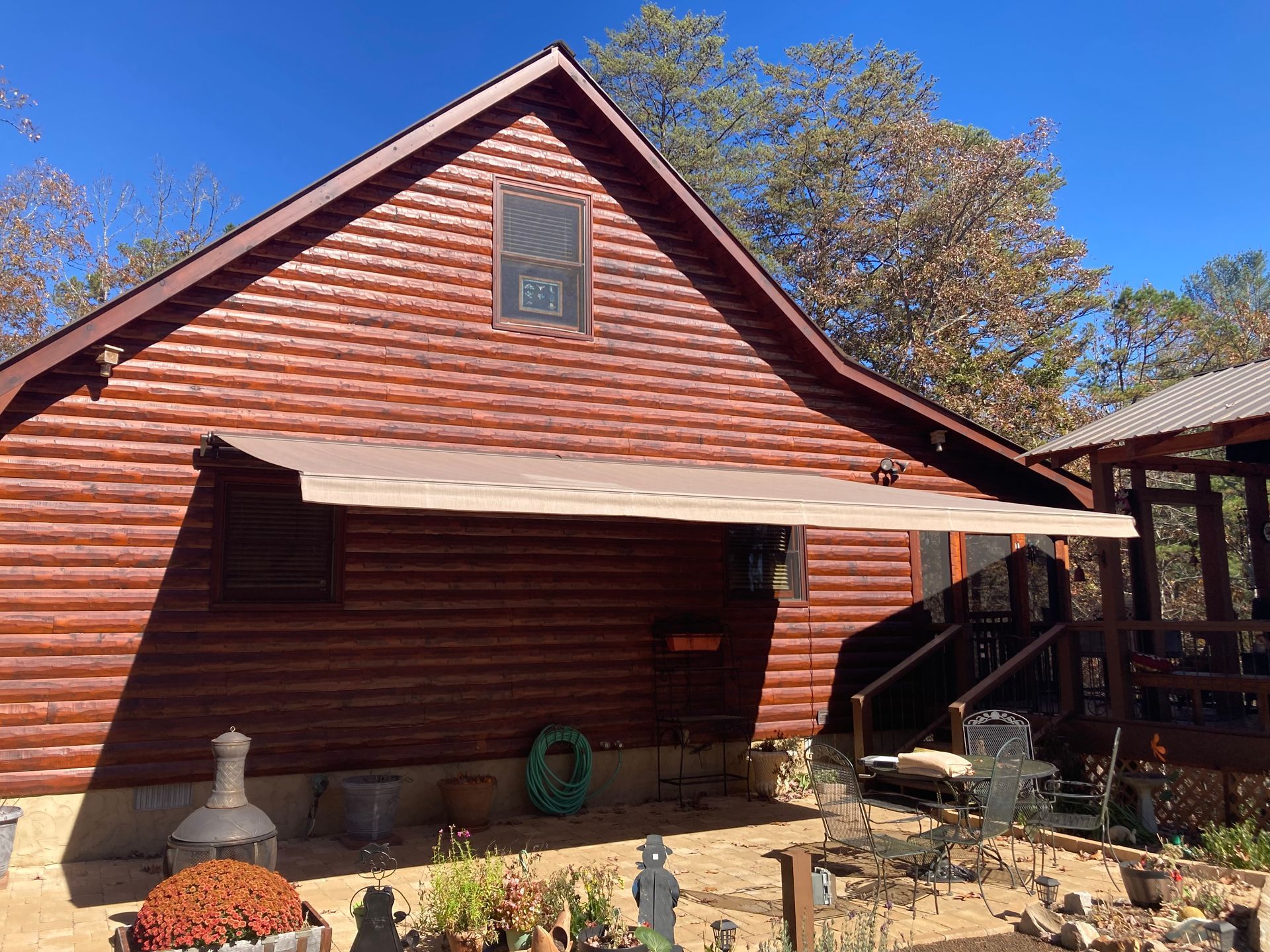 Log cabin with a tan retractable awning. Autumn leaves visible.