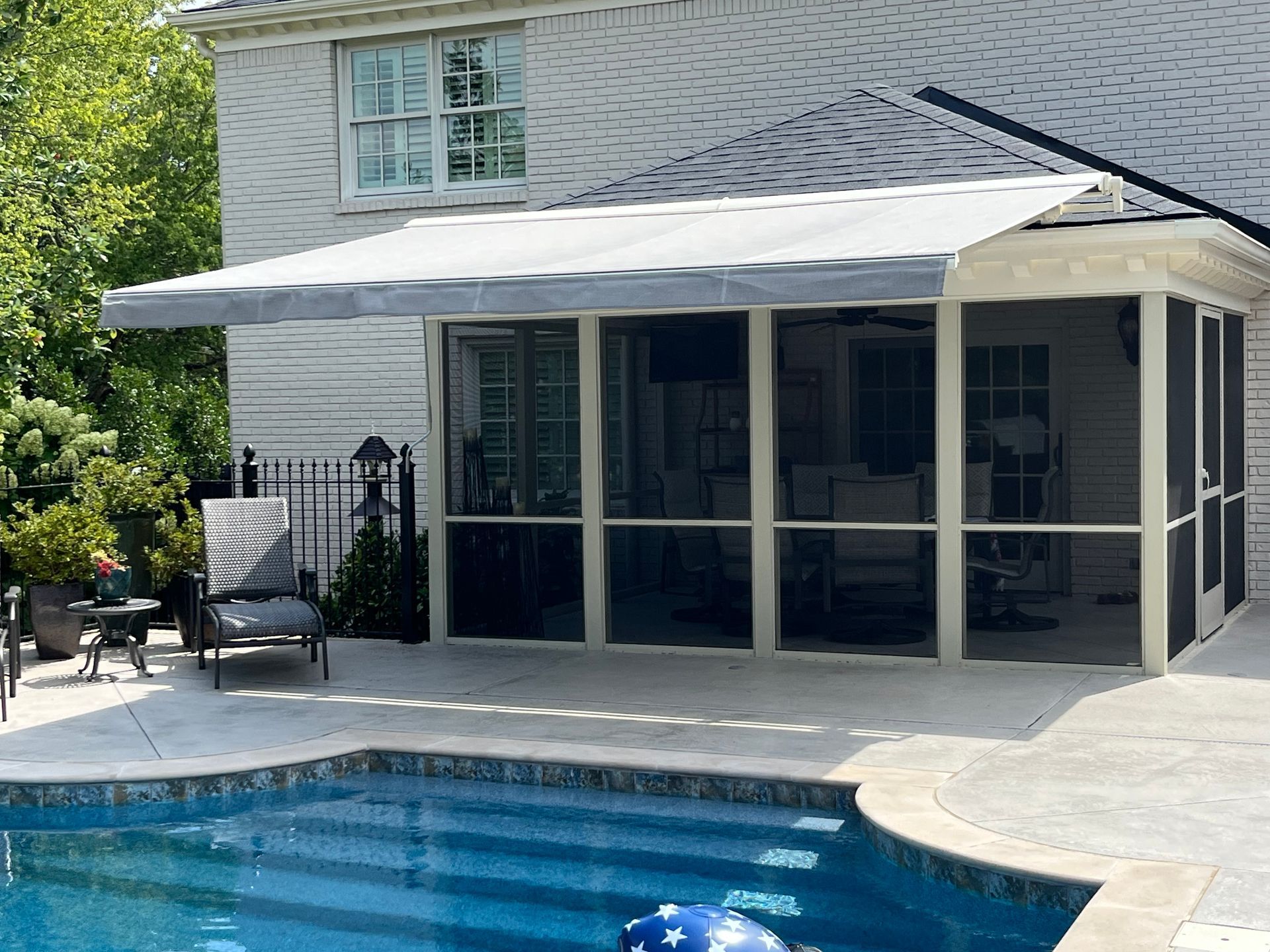 Poolside screened porch with retractable awning. Grey, light-colored, white house exterior.