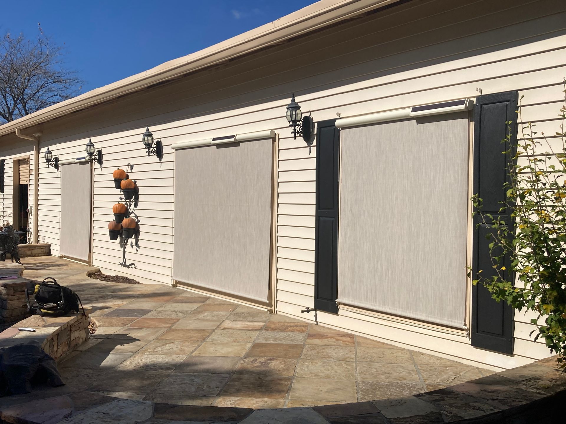 Exterior of a house with three retractable beige shades over openings, stone patio.