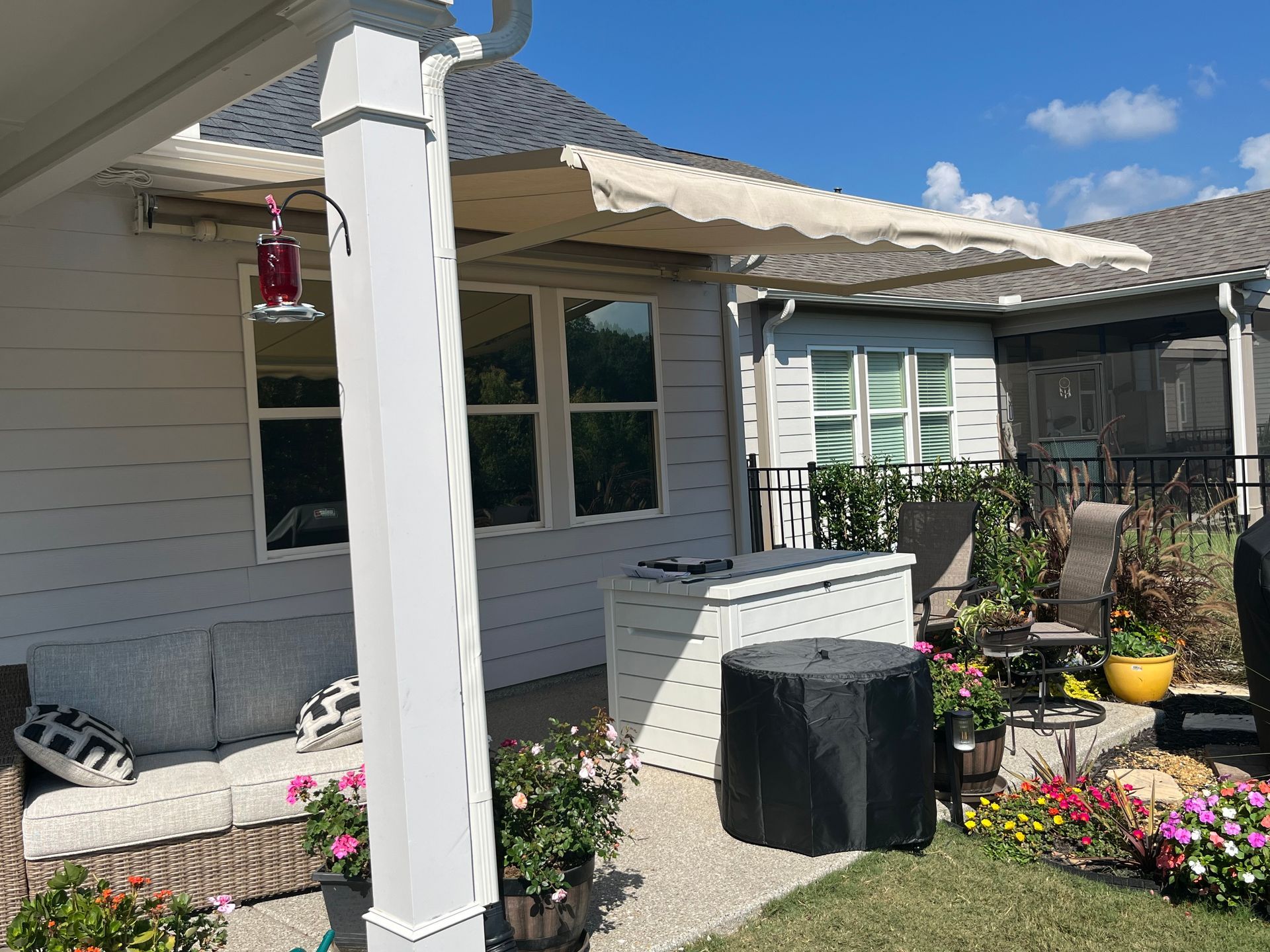 Patio with retractable awning, outdoor furniture, and flower garden on a sunny day.