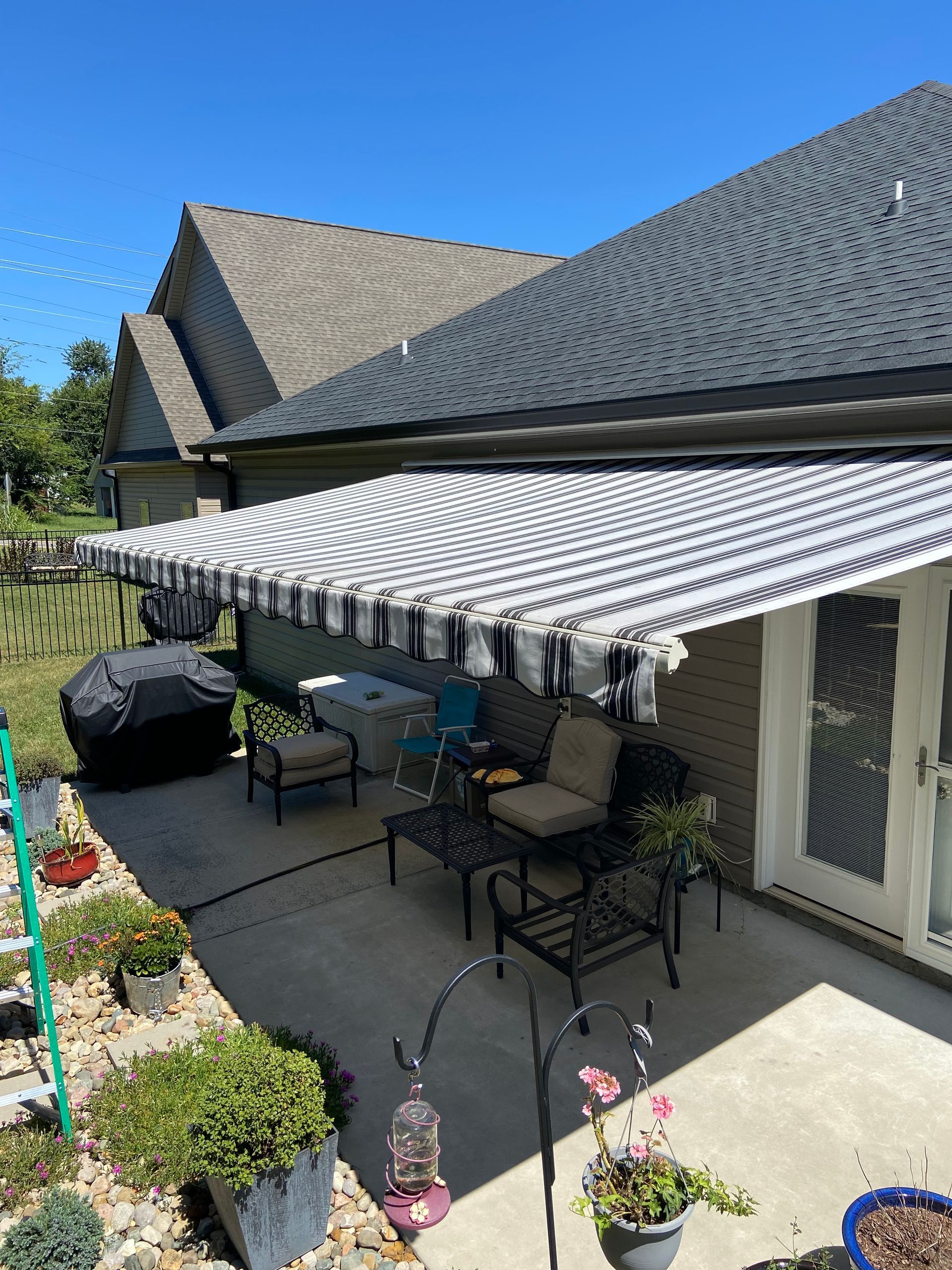 Patio with black and white striped awning, outdoor furniture, and potted plants. Sunny day.