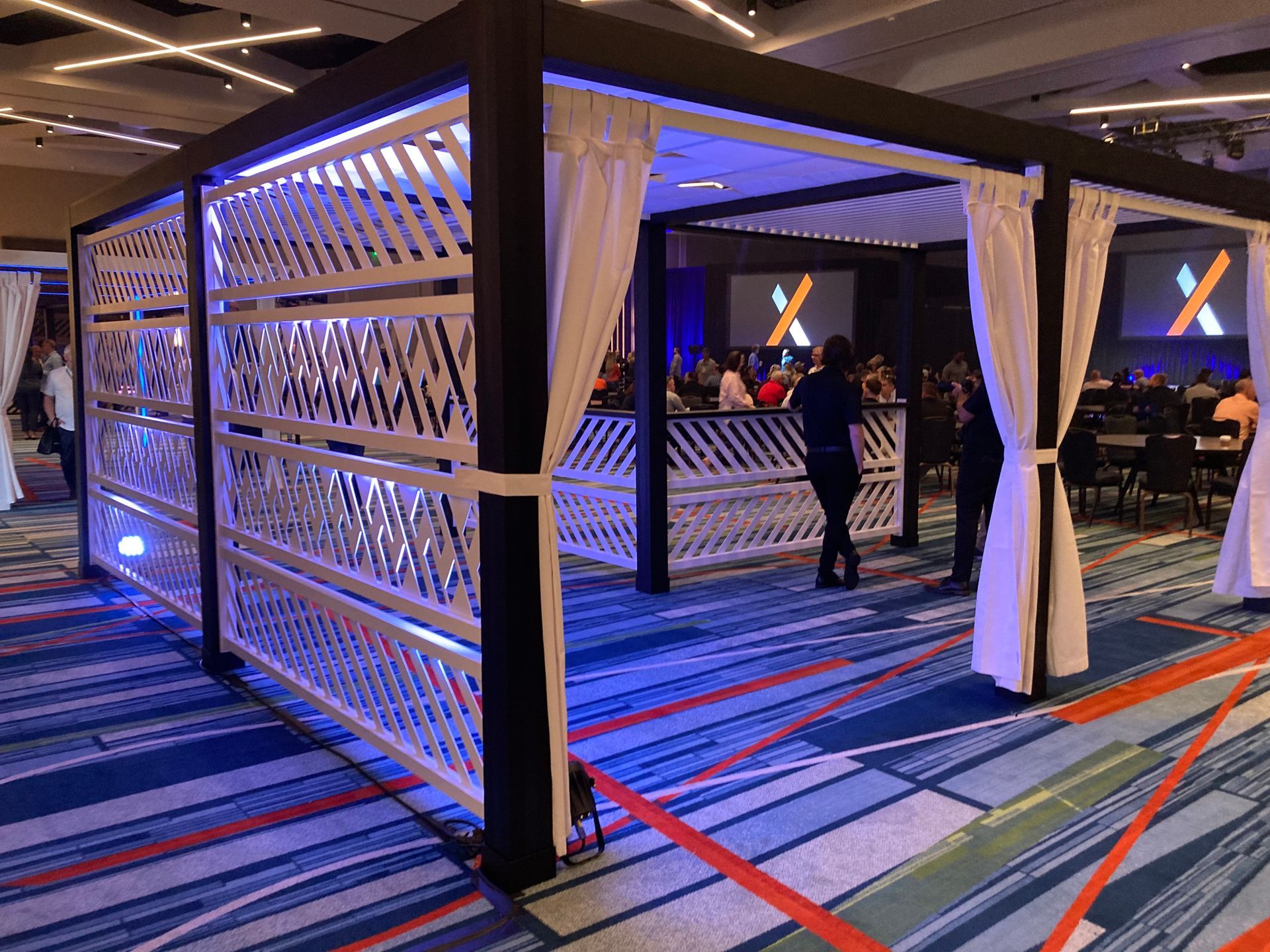 Event space with white lattice and black frame structure, blue LED lights, white curtains, and people.