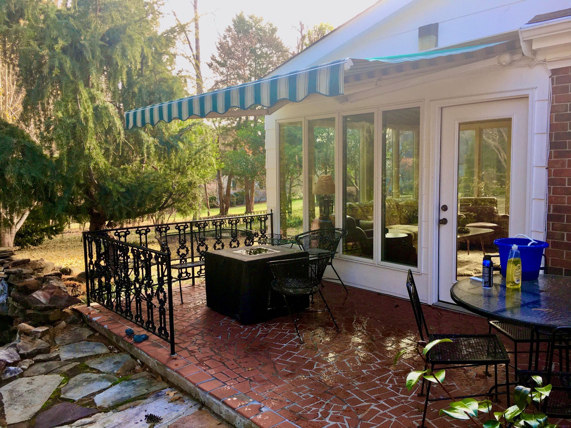 Patio with a brick building, awning, and black wrought iron railing and table set.