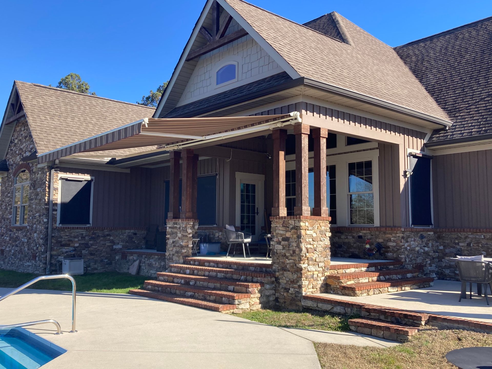 House with brick and stone facade, covered porch, retractable awning, and a pool.