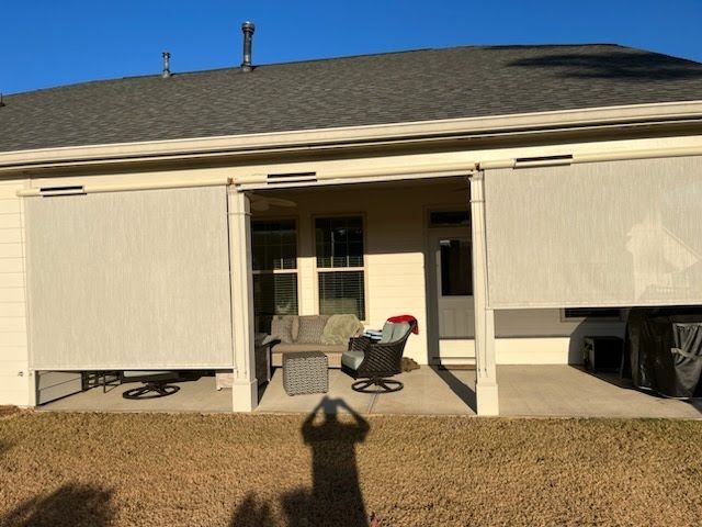 Patio with beige sun shades, outdoor seating, and a house. Shadow of person taking photo.