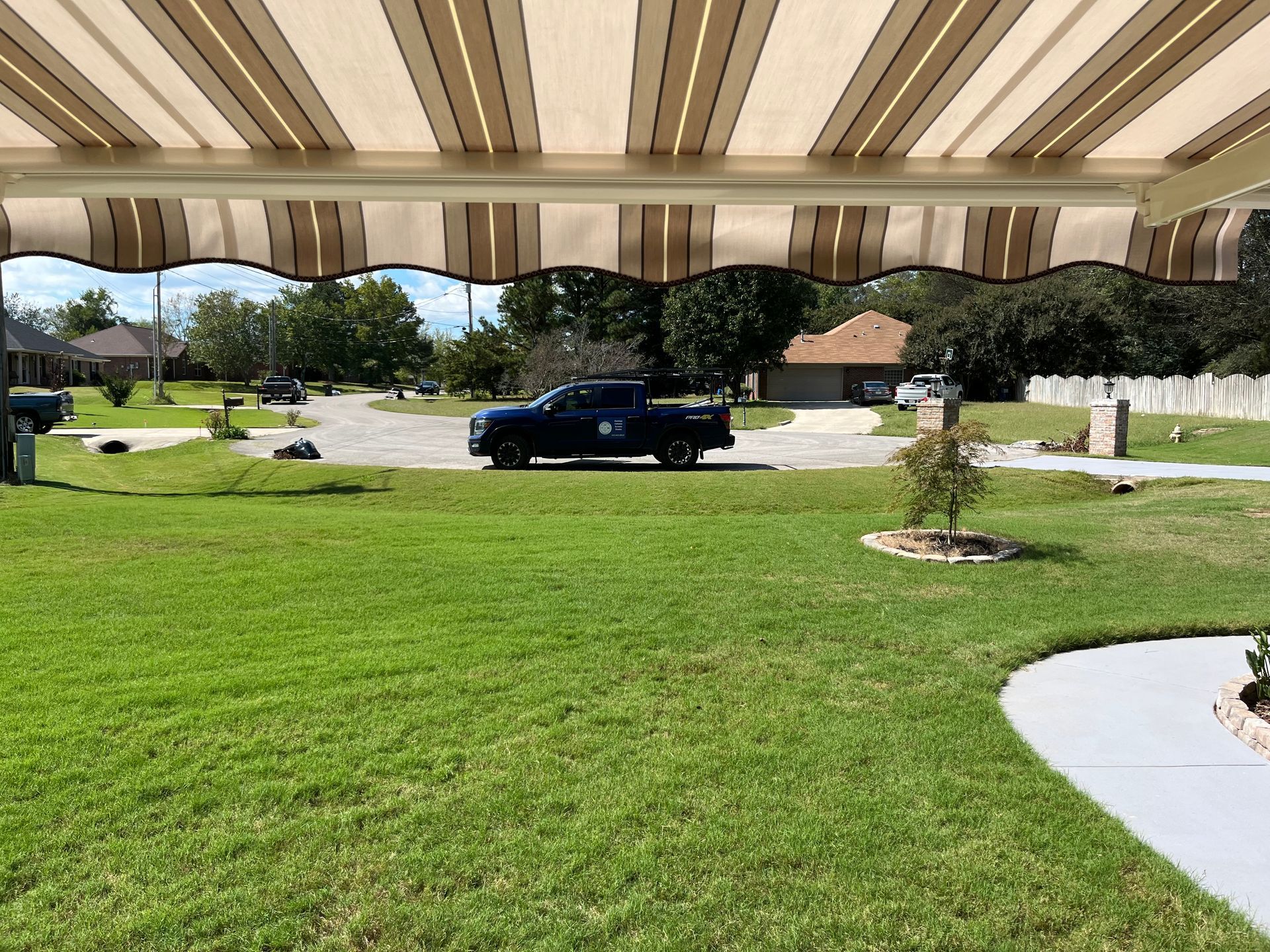 View from under a striped awning, overlooking a green lawn with a truck parked in the distance.