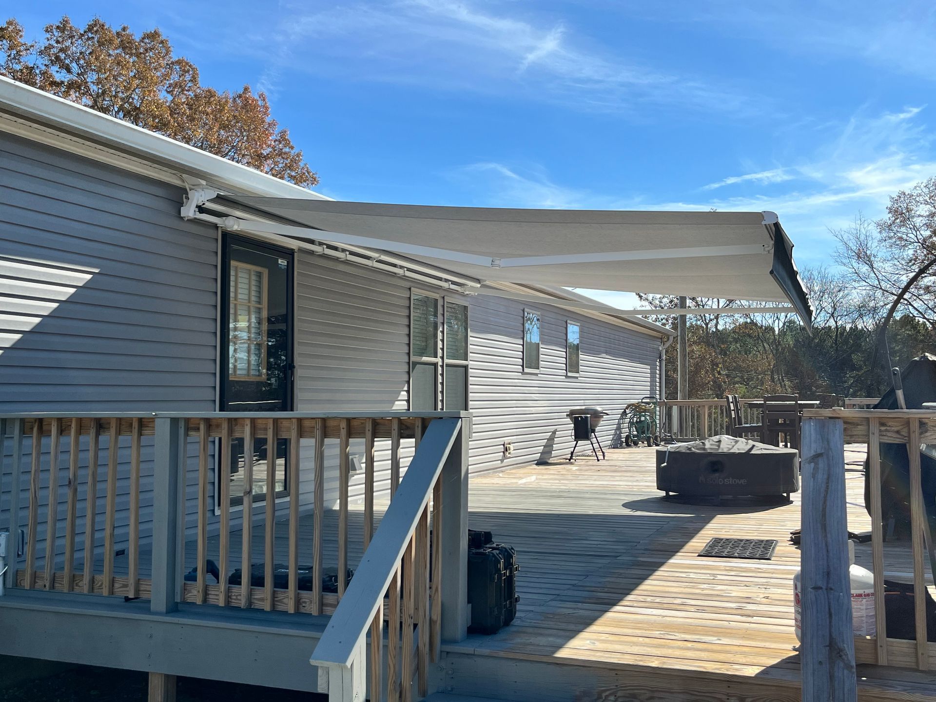 Gray house with extended awning over a wooden deck on a sunny day.