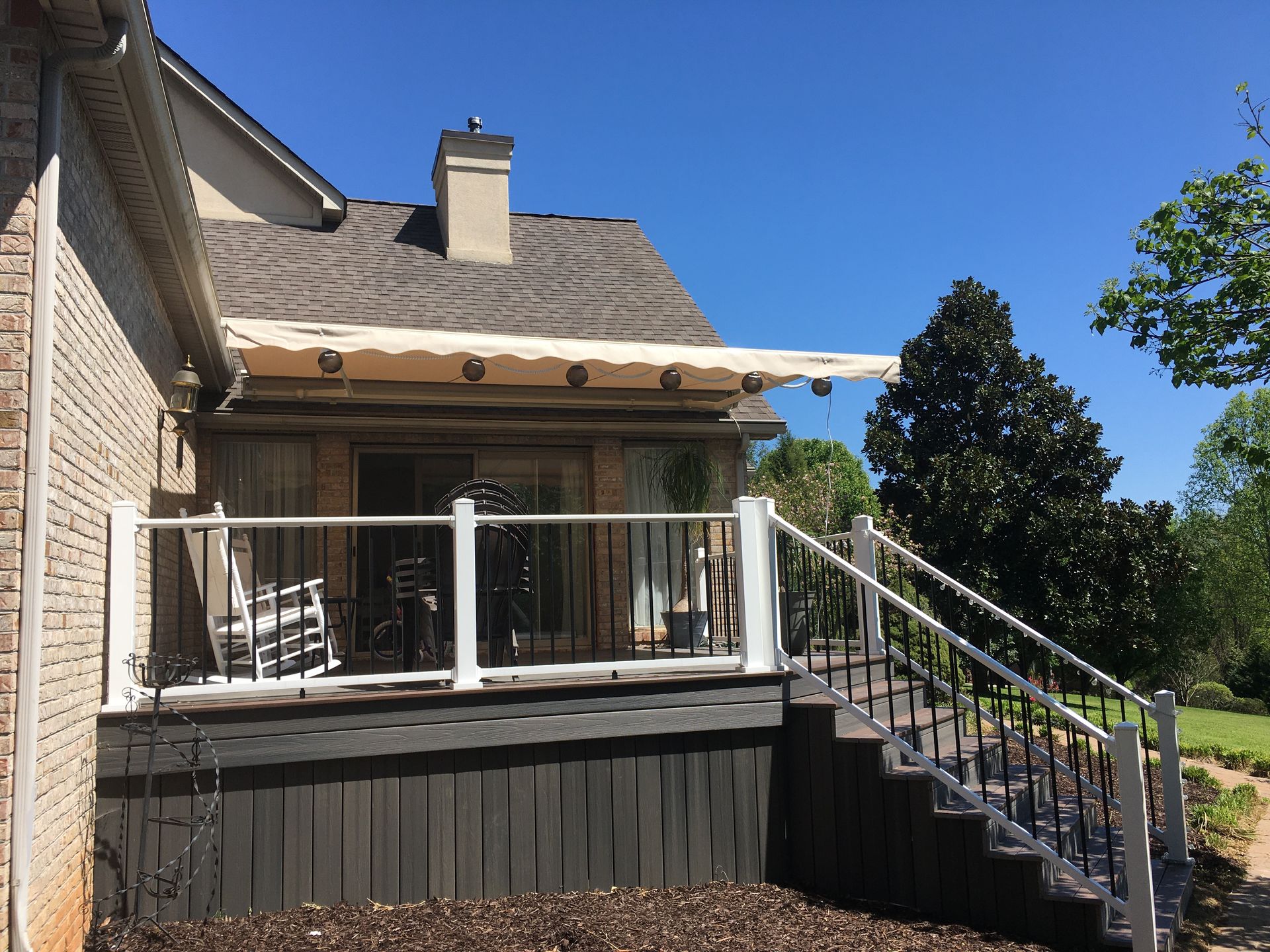 Deck with retractable awning over a glass door, next to a brick house and steps leading up.