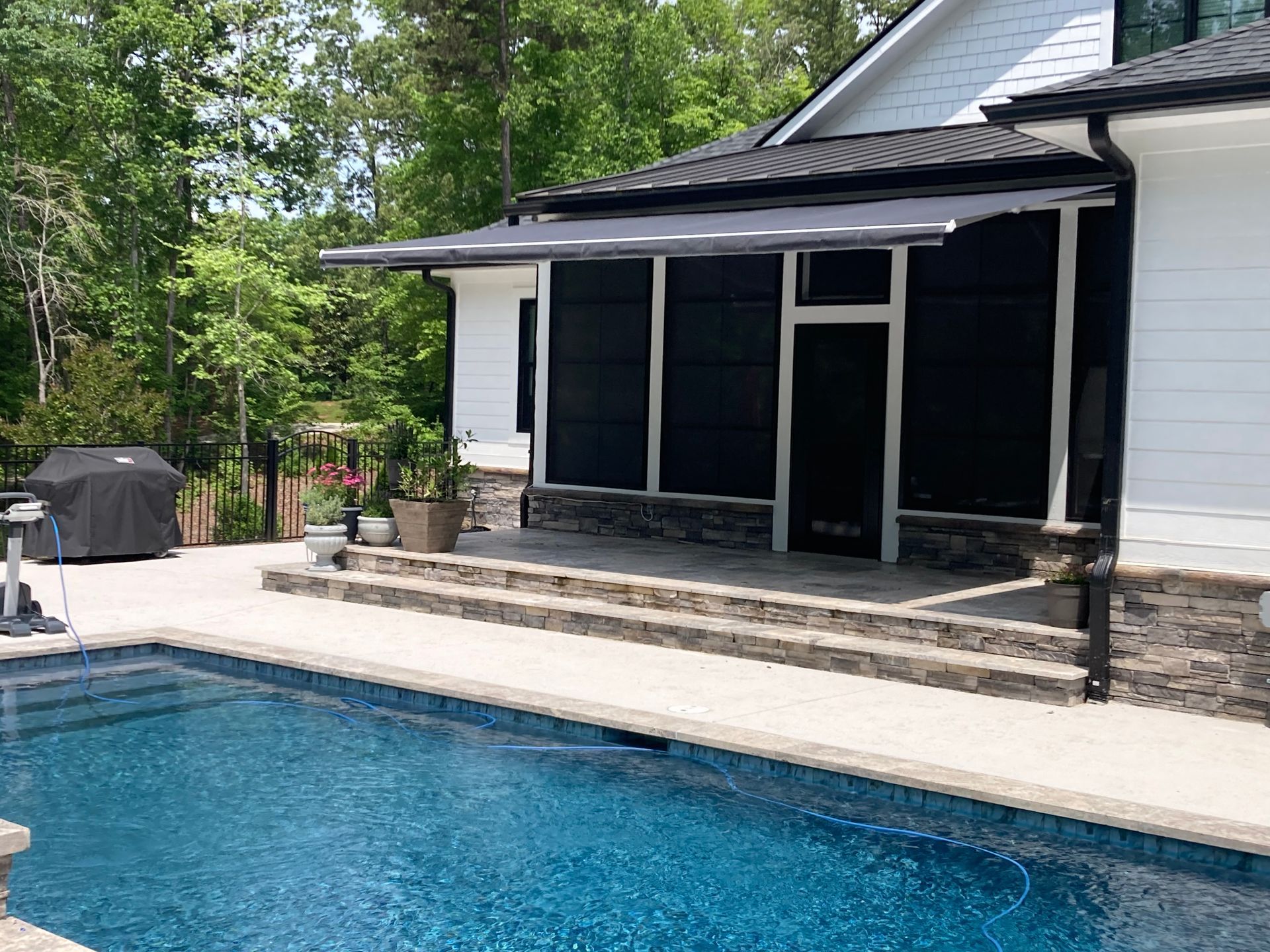 Poolside patio with retractable awning; a screened-in porch with dark screens; stone steps leading to the patio.