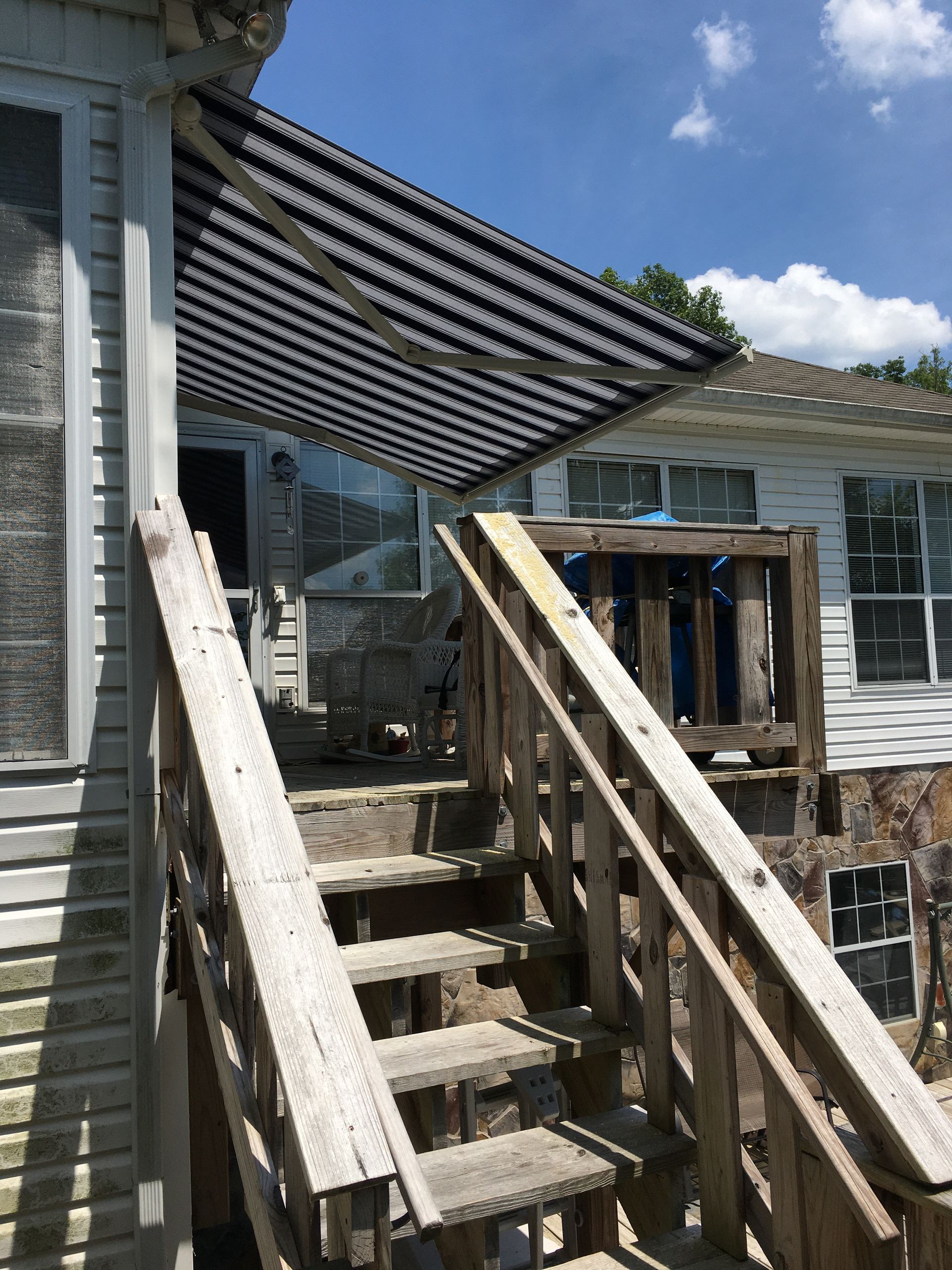 Wooden stairs leading to a porch with a striped awning. The house is weathered. Blue sky in the background.
