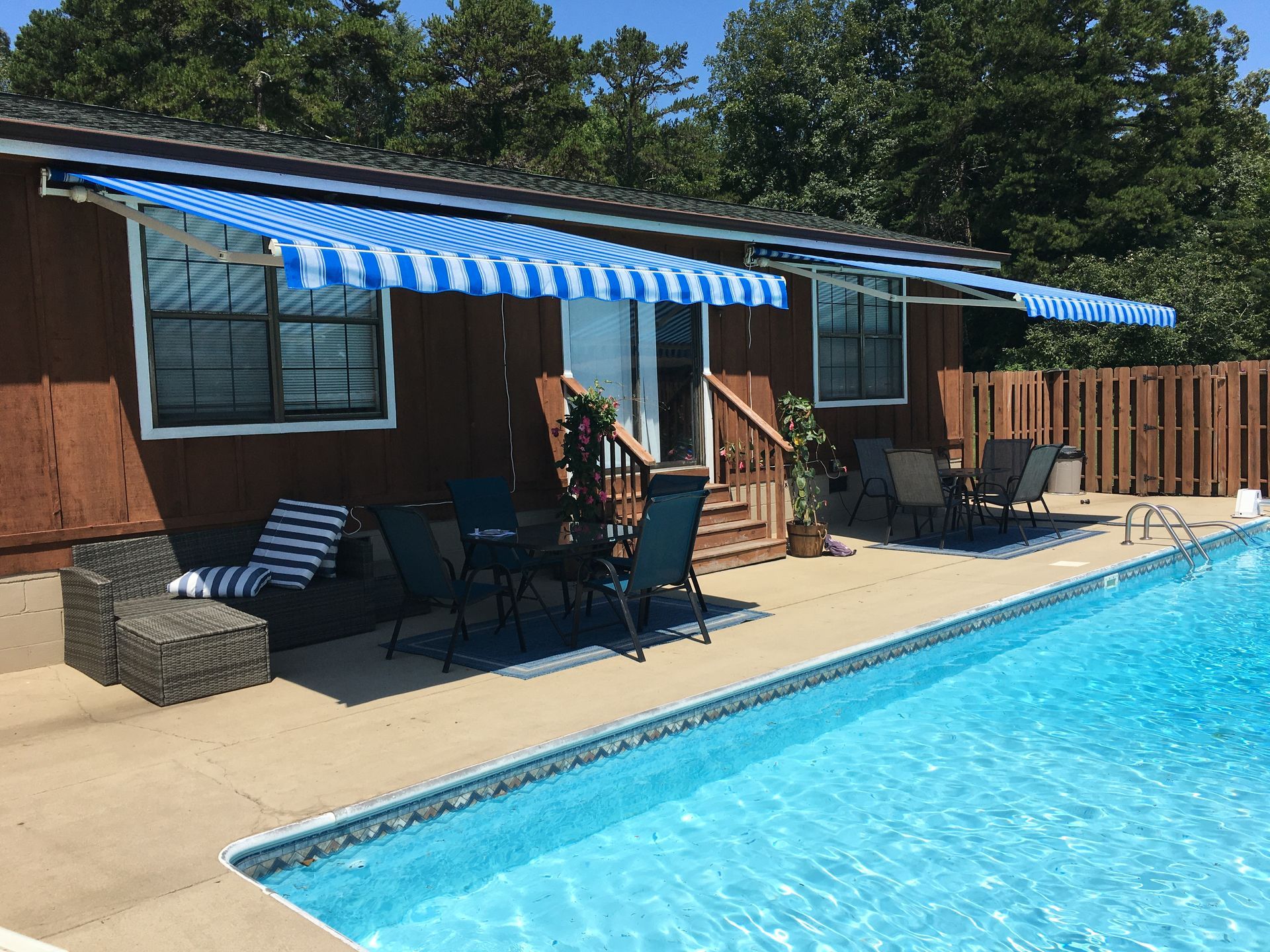 Poolside patio with blue and white striped awnings, pool, chairs, and dark brown siding.