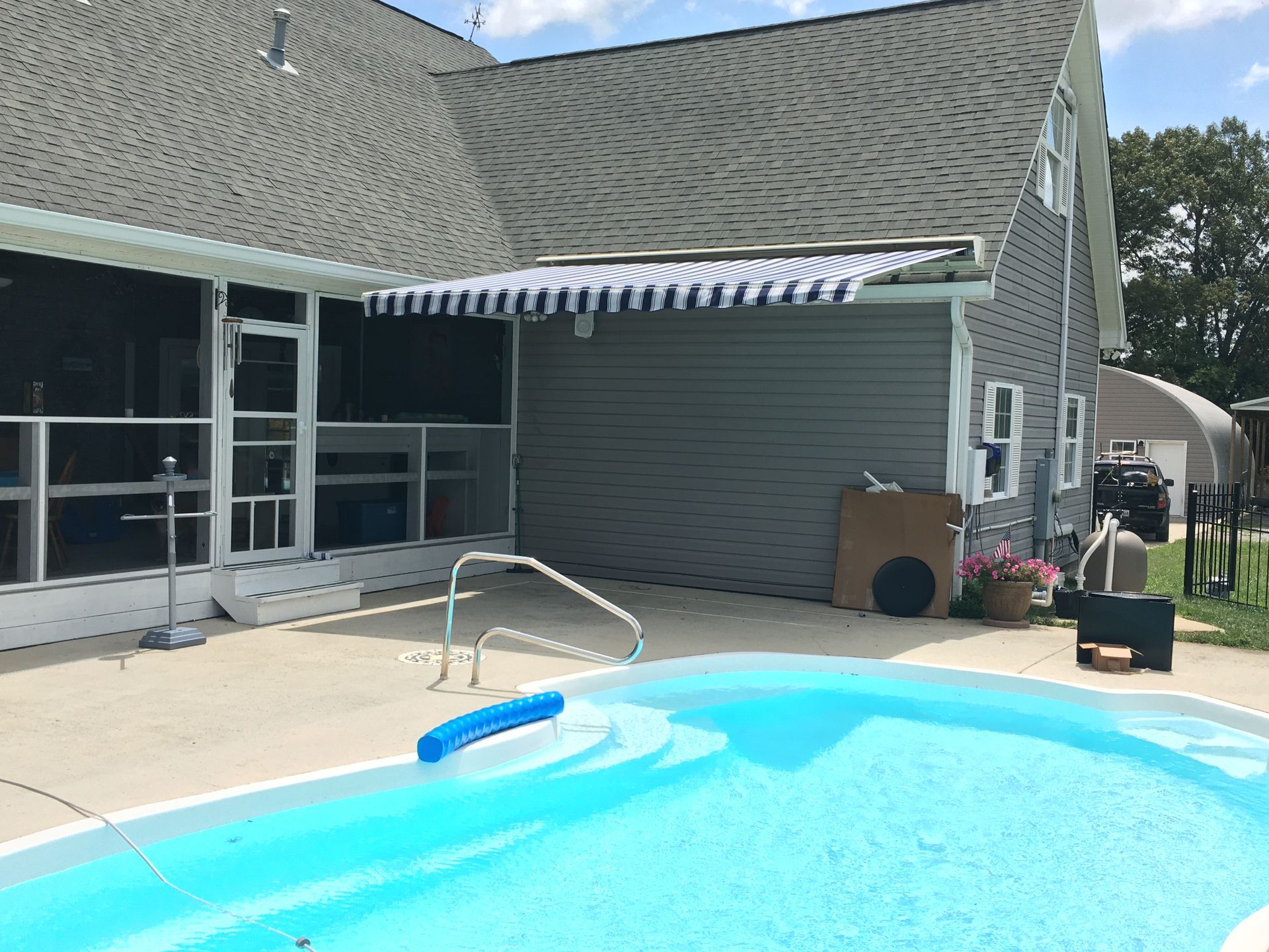 A swimming pool with blue water next to a house with a retractable striped awning.