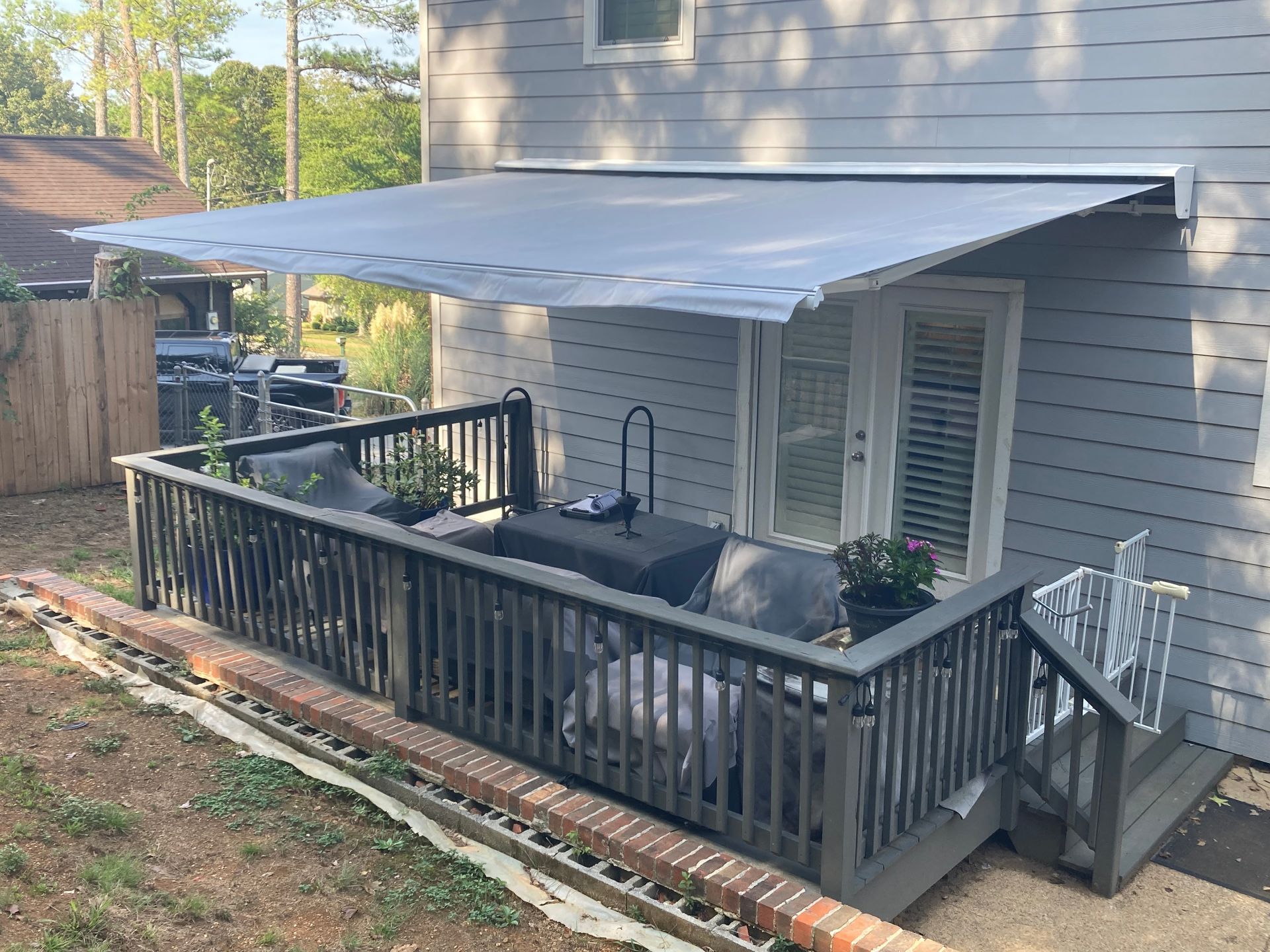 Deck with retractable awning over outdoor seating, next to a house.