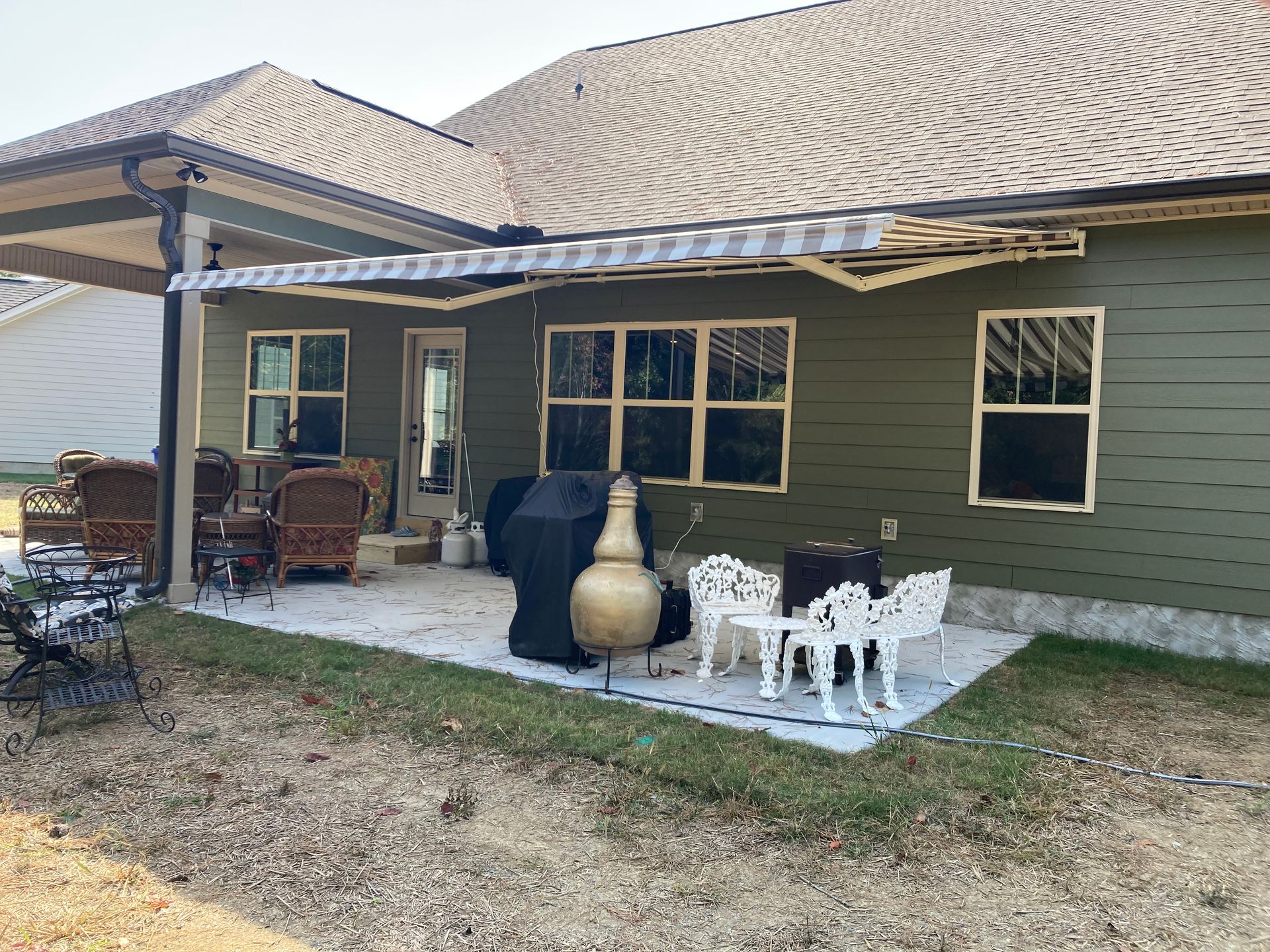 Backyard patio with green siding, awning, and outdoor furniture.