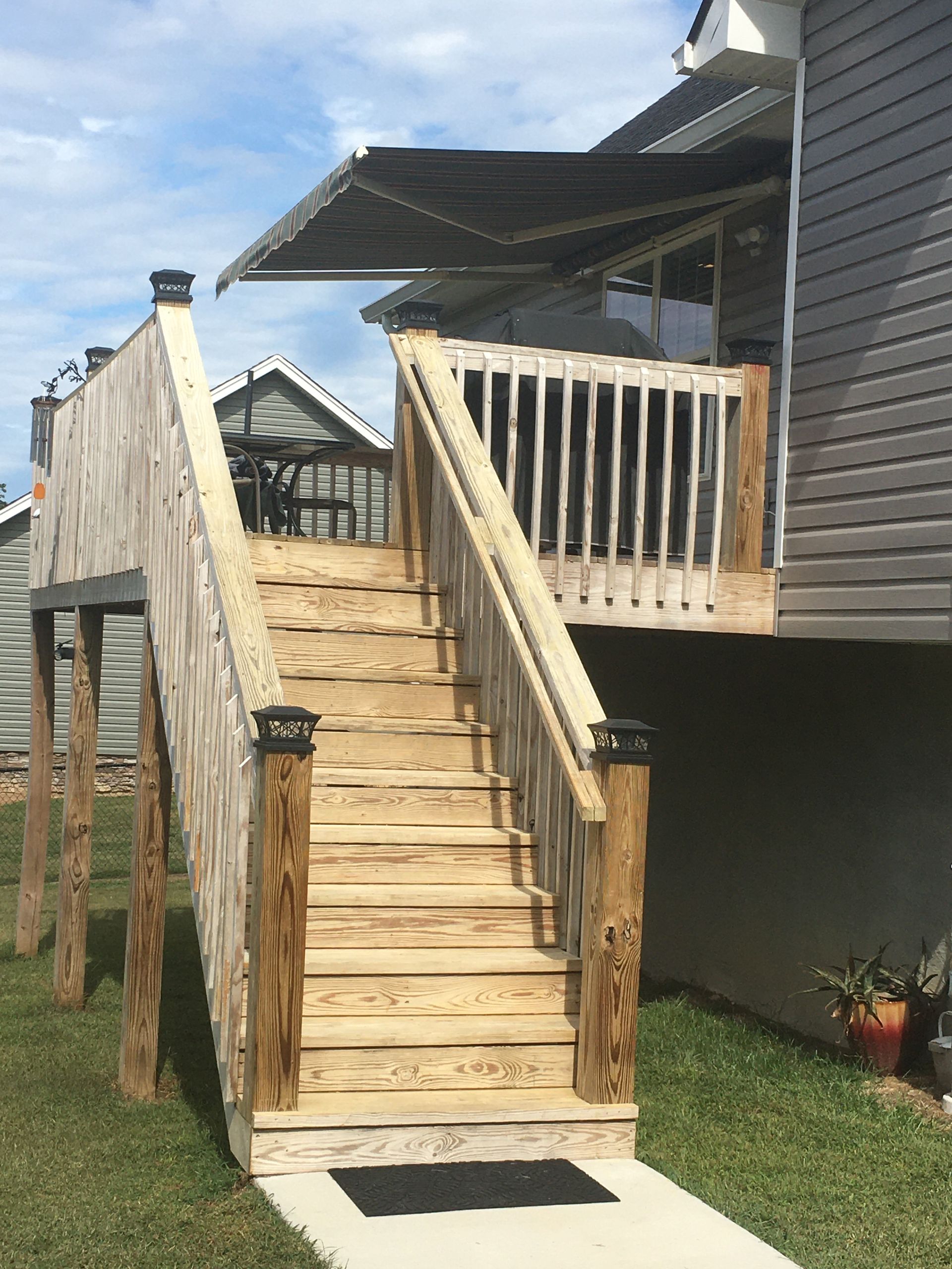 Wooden staircase leading up to a deck attached to a house. An awning shades the deck.