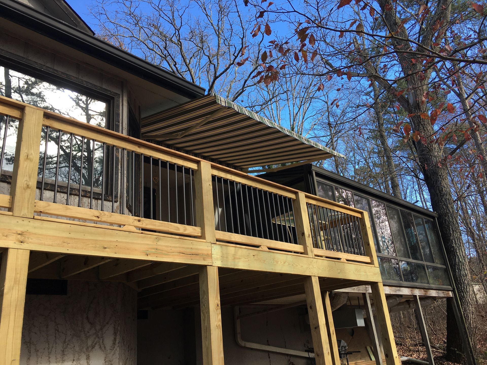 Wooden deck with awning, overlooking trees and a blue sky.