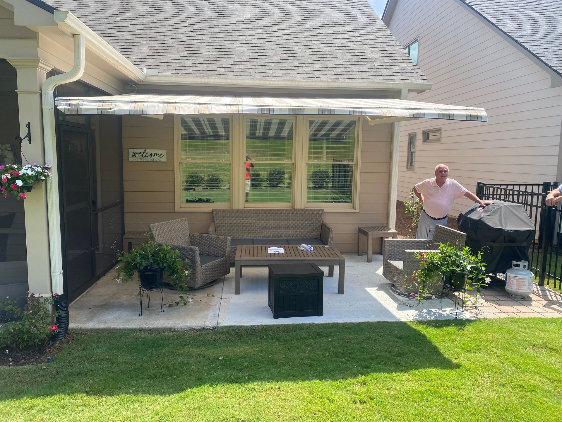 Patio with outdoor furniture, awning, and person grilling near a house.