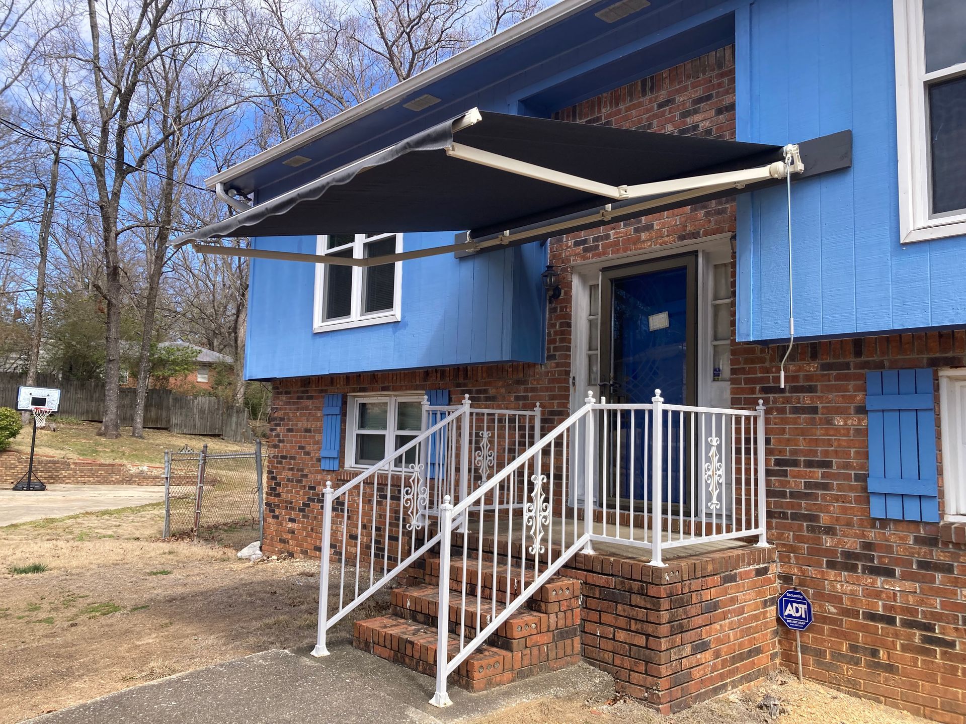 House with blue siding and an awning over the front door, with stairs and a white railing.