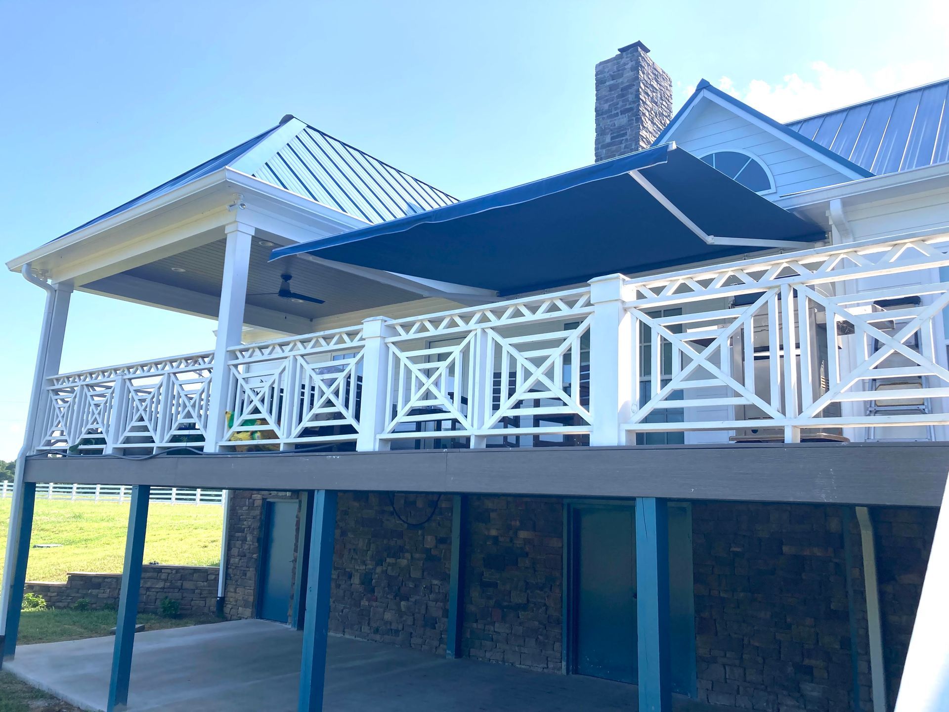 Deck with a blue awning and white railing, attached to a house with a blue roof.