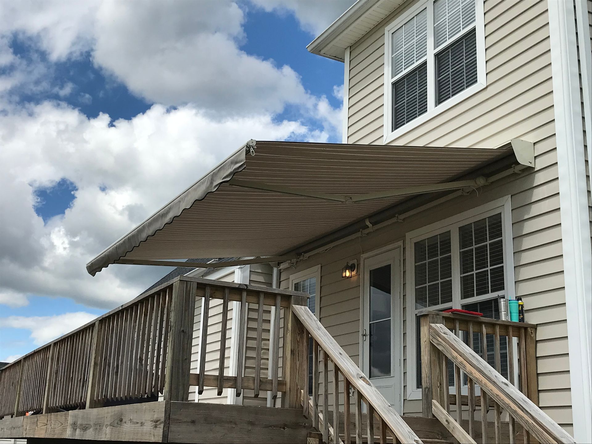 Beige awning over a deck door, attached to a light-colored house. Wooden deck and stairs in the foreground.