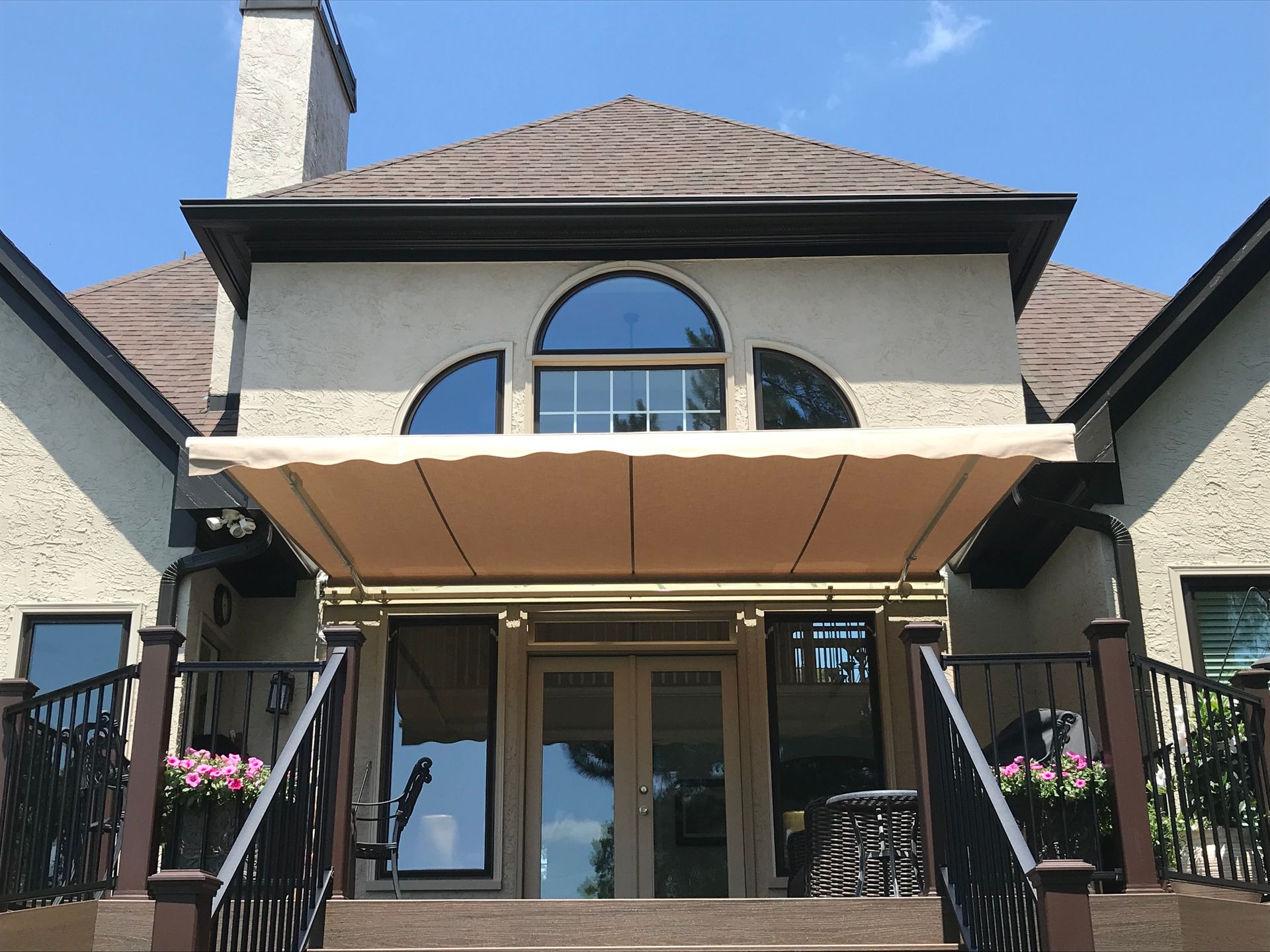 Tan awning over a doorway of a stucco house with black railings and a deck.