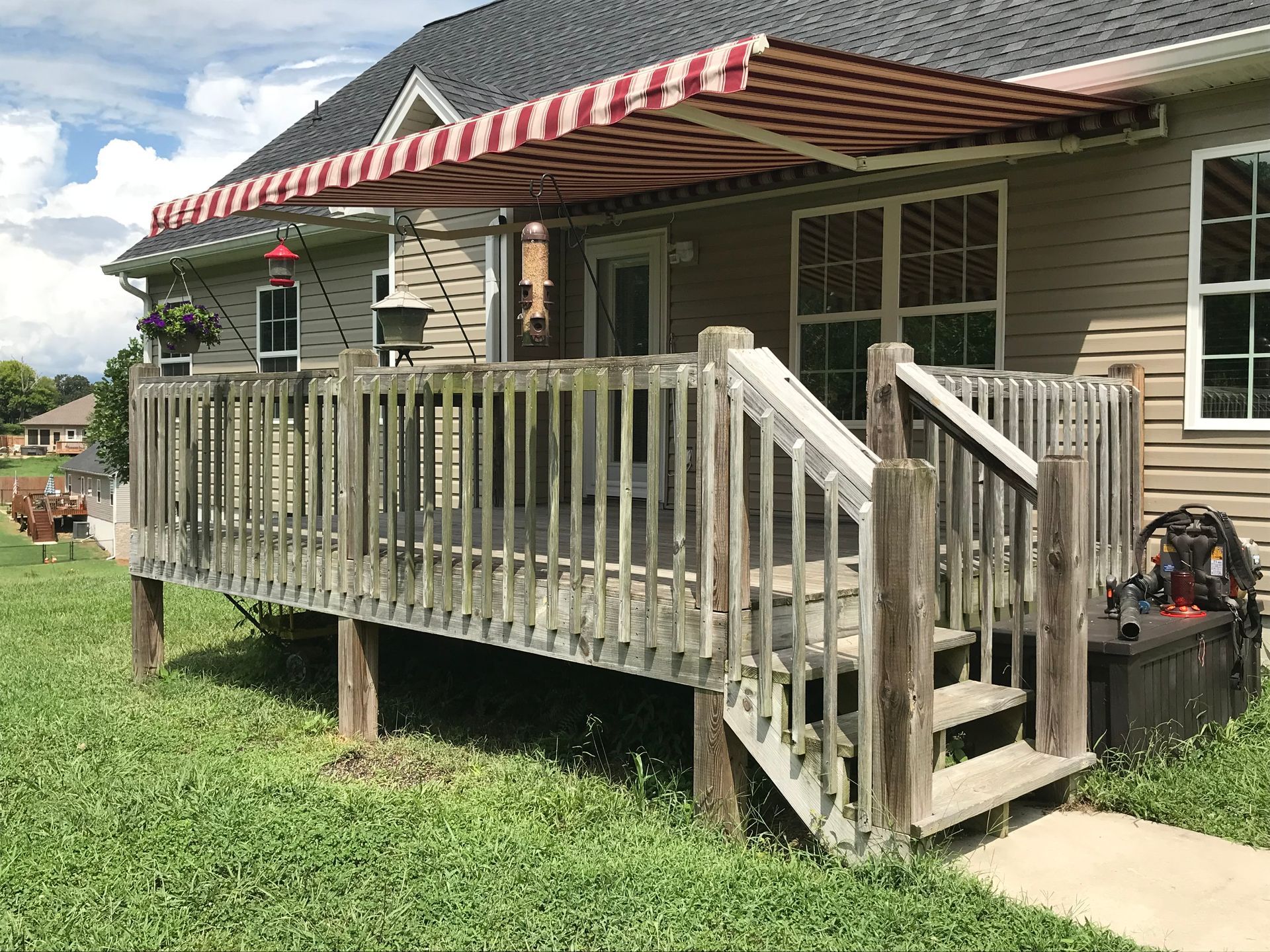 Deck with red and white striped awning extending from a beige house.