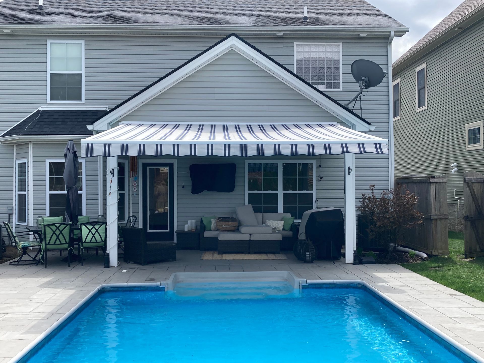 Backyard patio with striped awning, outdoor seating, and a swimming pool.