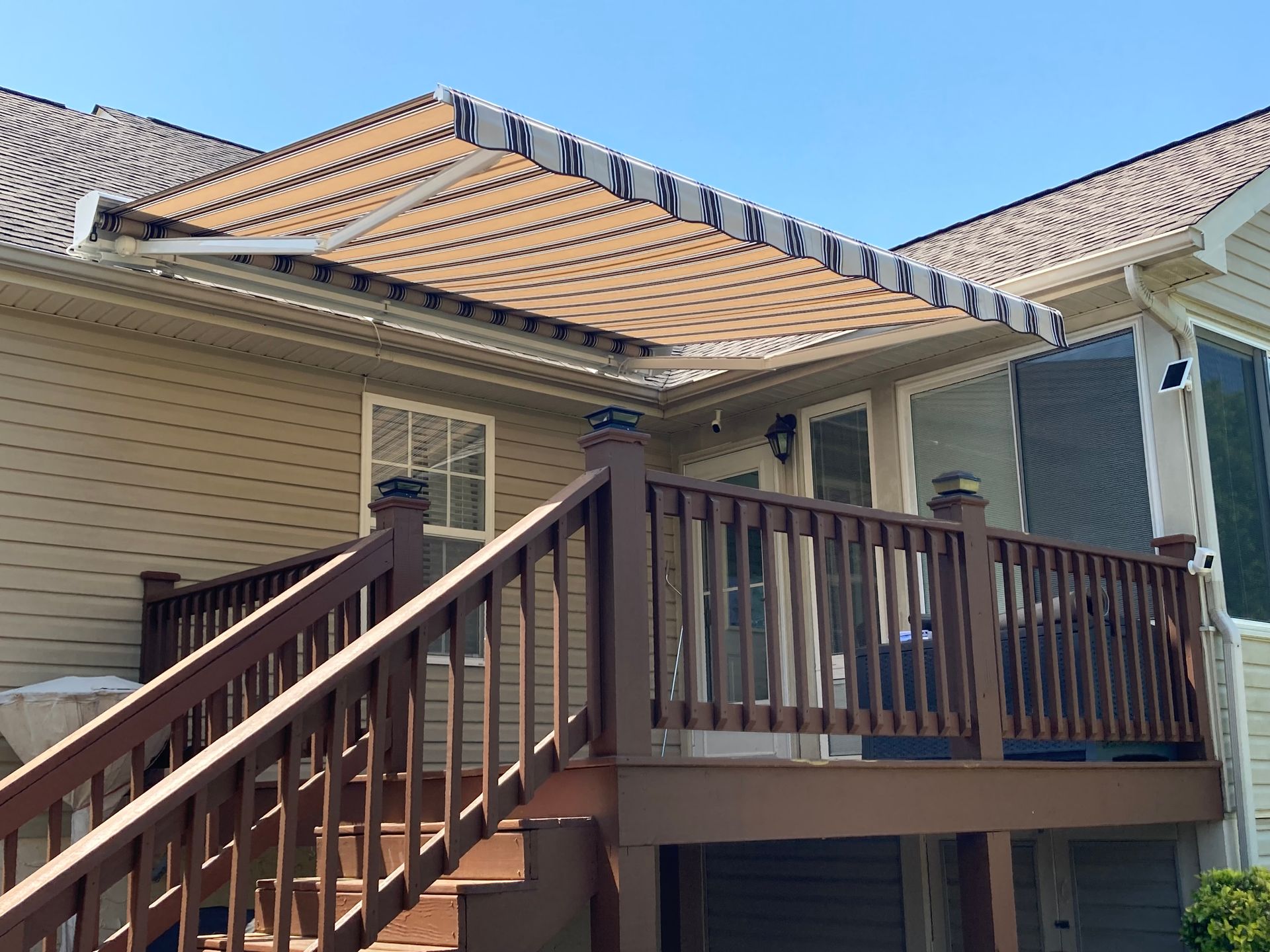Deck with brown railing, awning over sliding doors, tan and blue stripes.