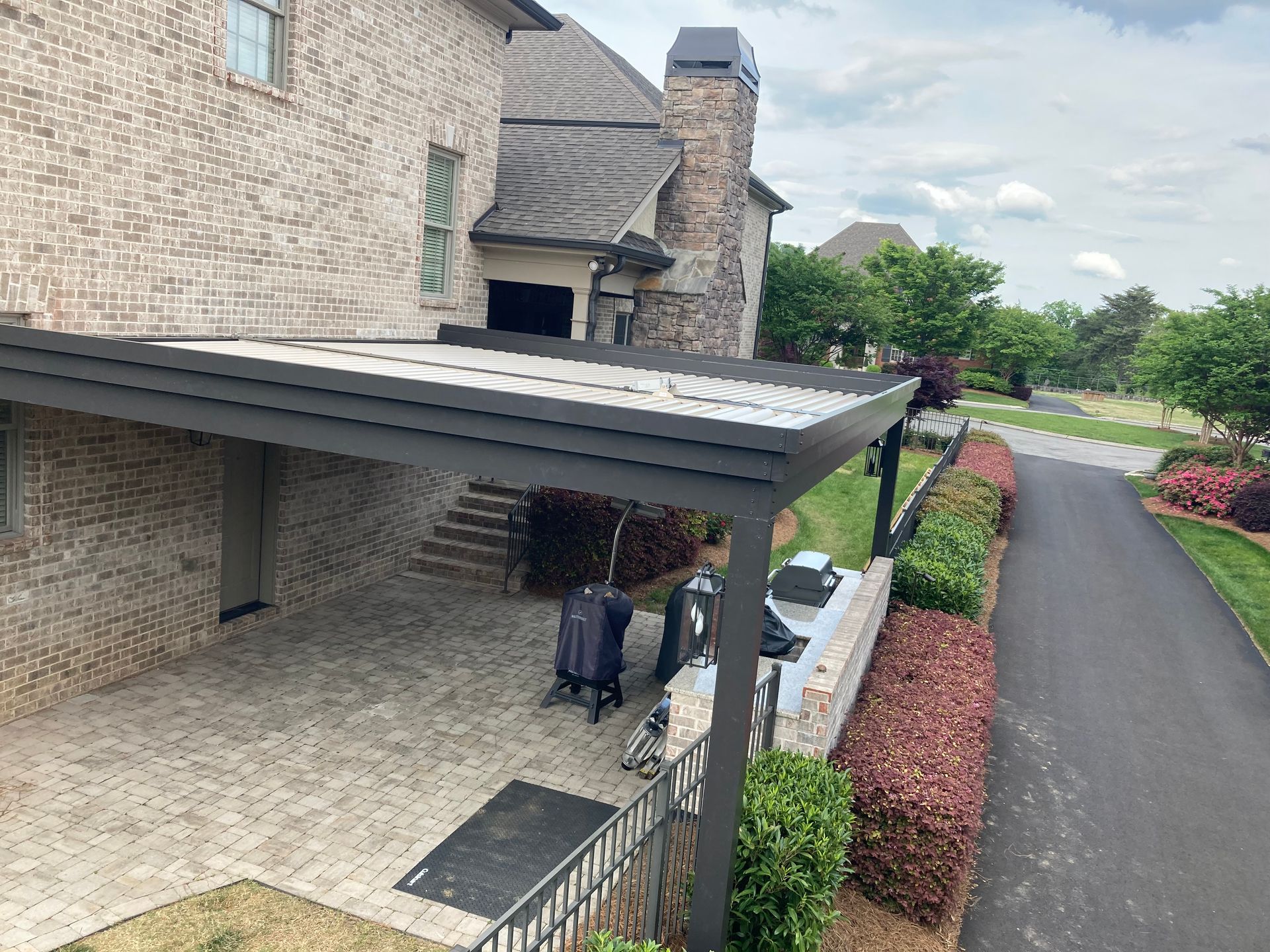 Patio with black canopy, brick house, barbecue, and walkway with greenery.