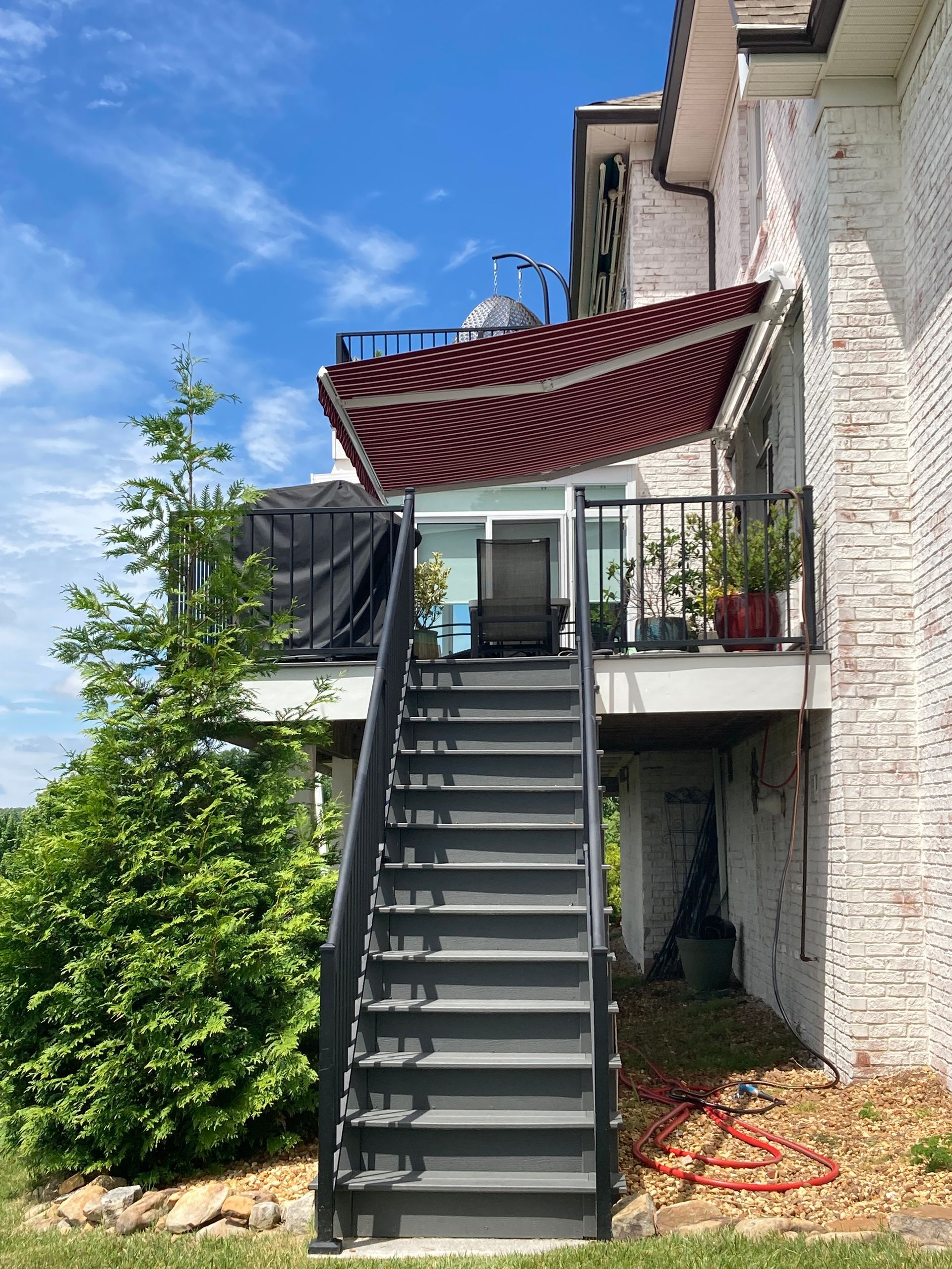 Staircase leading to a second-story deck with a striped awning, next to a white brick building, sunny day.