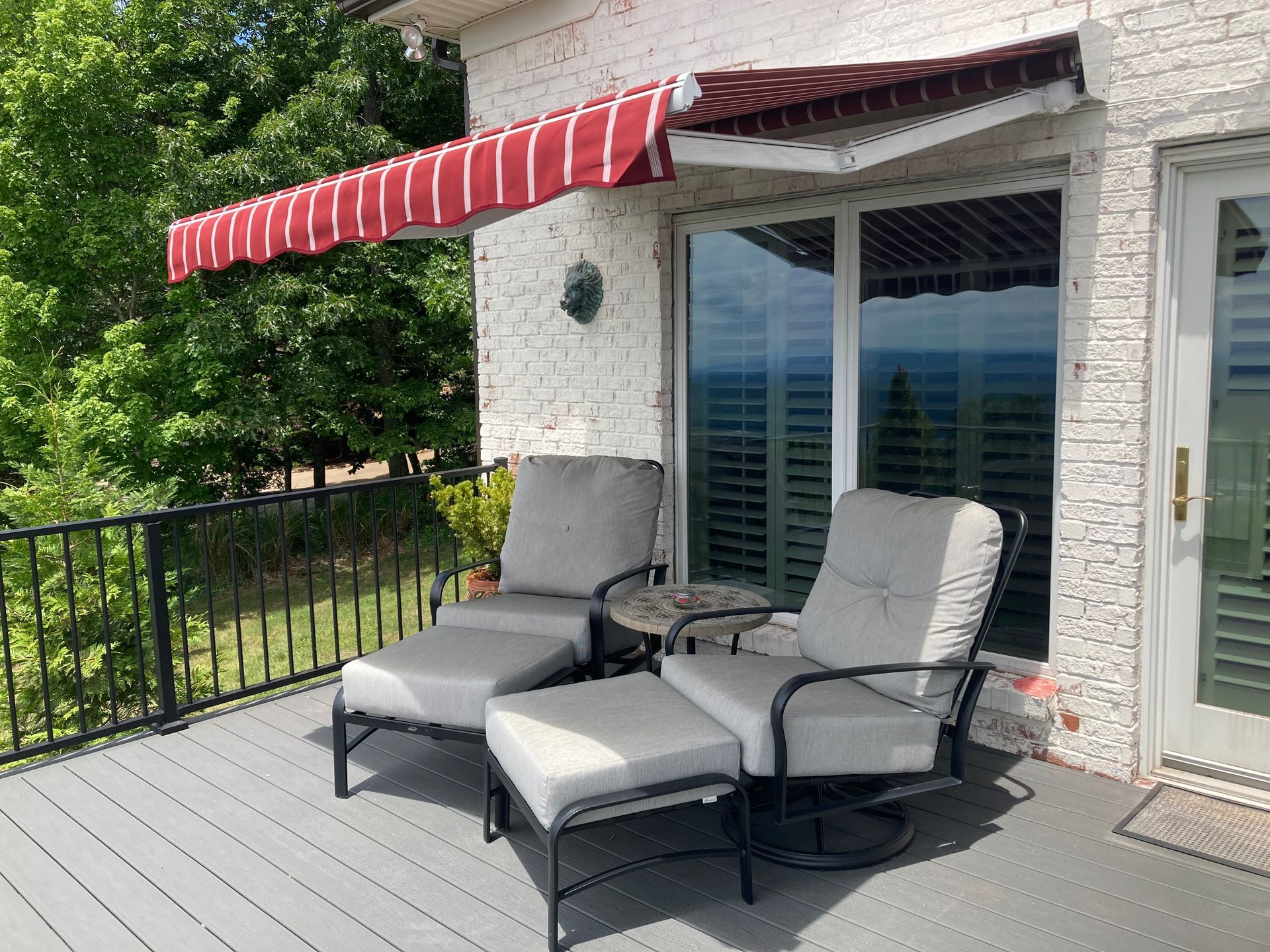 Patio with lounge chairs, small table, awning, and sliding glass door. Red and white awning provides shade.
