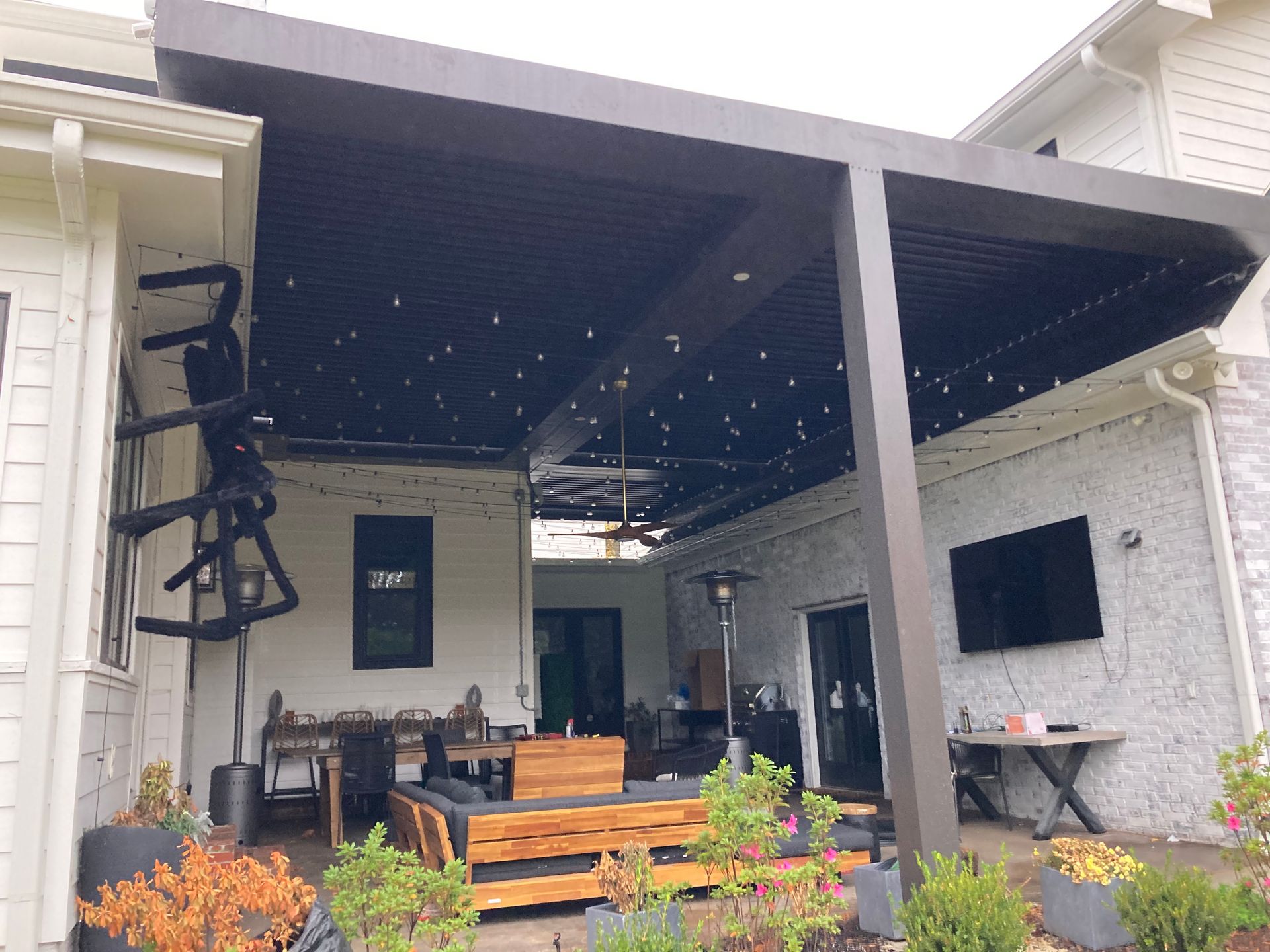 Covered patio with seating, string lights, and a TV on the exterior of a house.