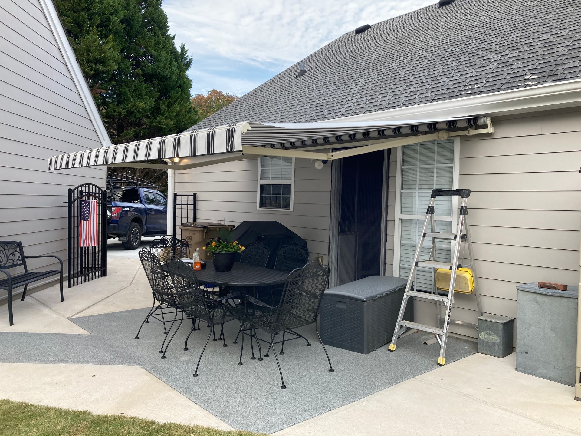 Patio with retractable awning, table, chairs, door, and ladder. Gray and beige tones.