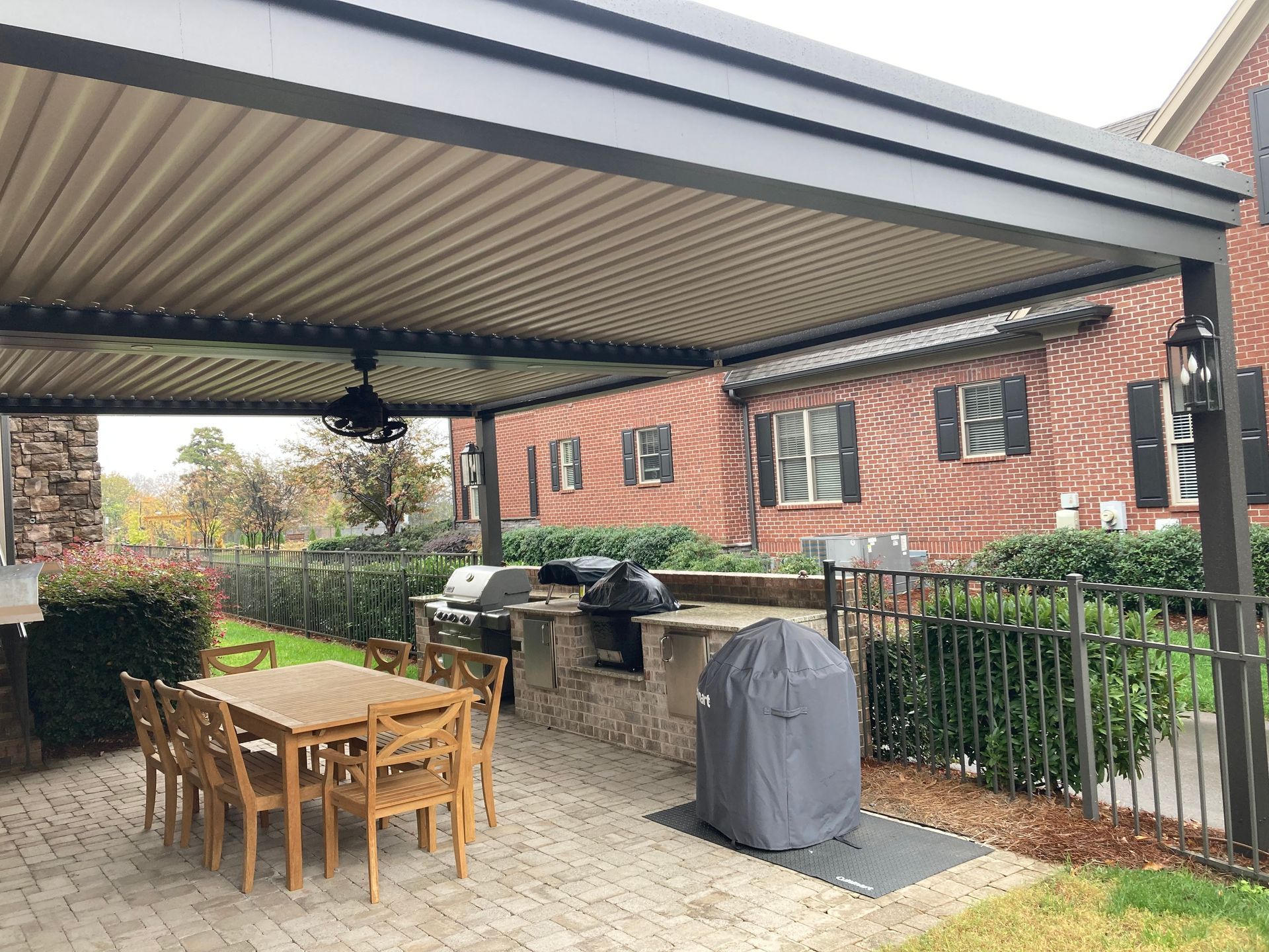 Outdoor kitchen with dining set, grill, and covered patio in front of a brick building.