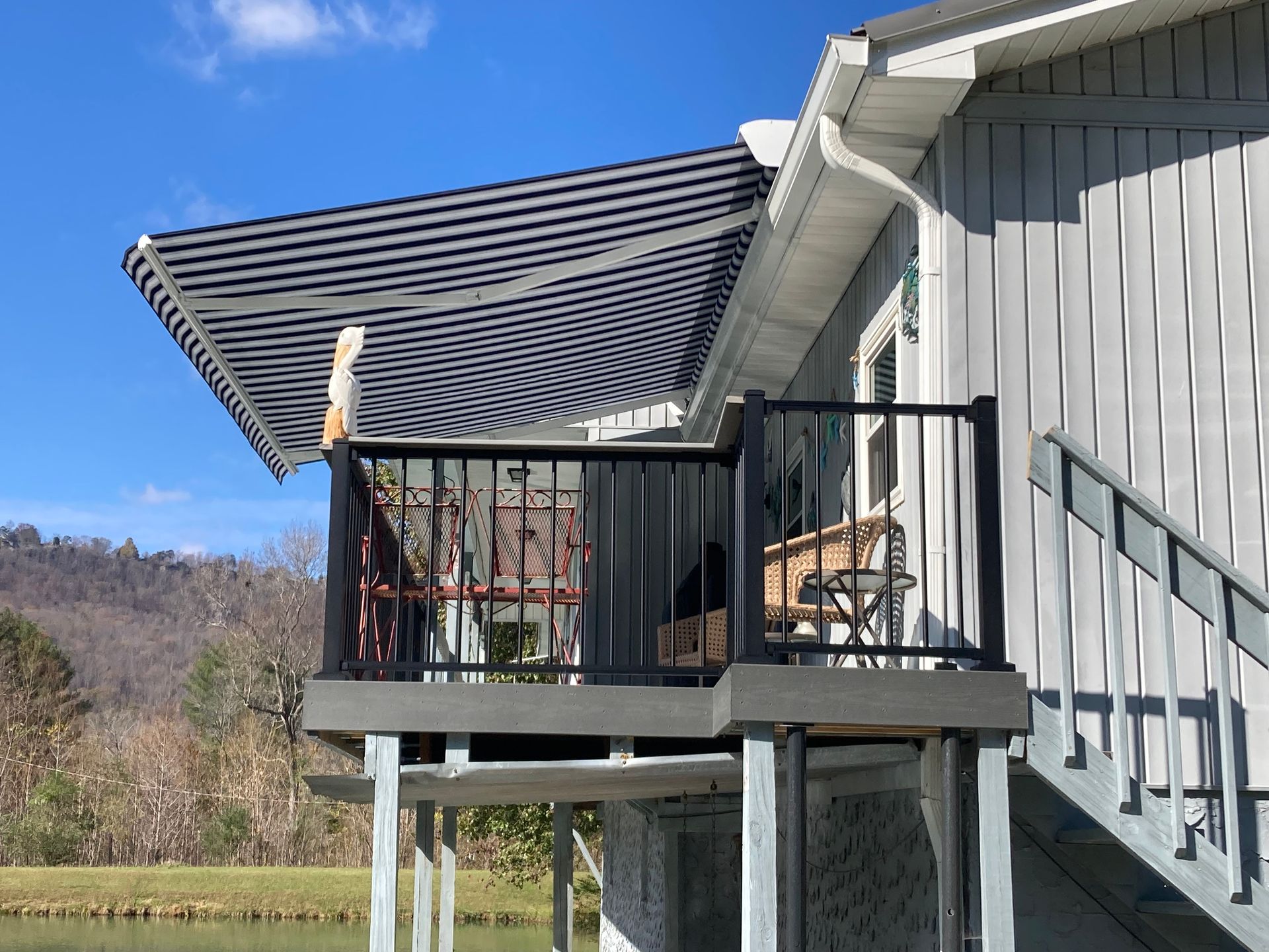 Blue and white striped awning over a deck on a light gray house. Black railing and stairs.