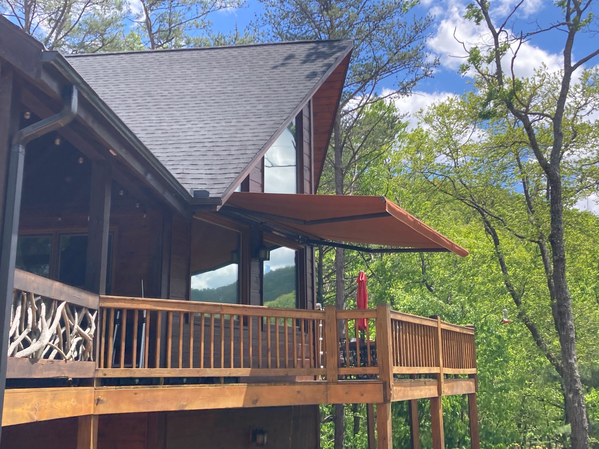 Wooden cabin with deck and retractable awning, surrounded by trees.