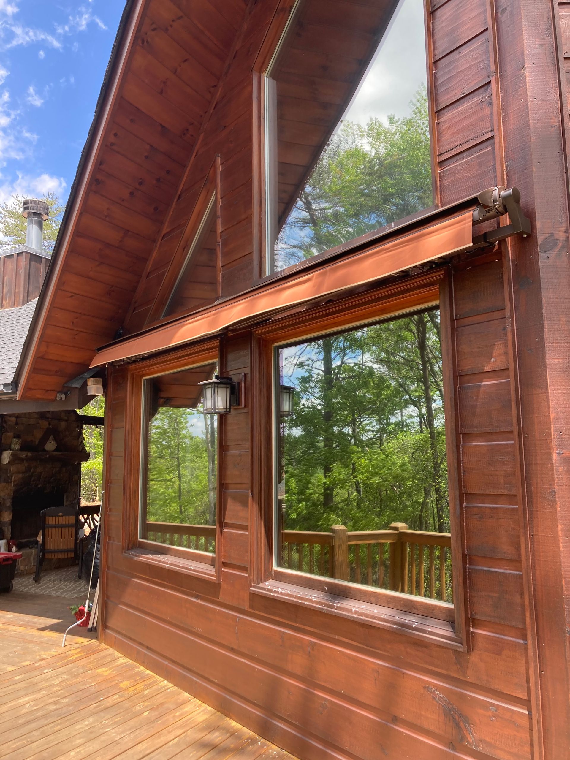 Brown wooden house with large windows reflecting trees and blue sky.