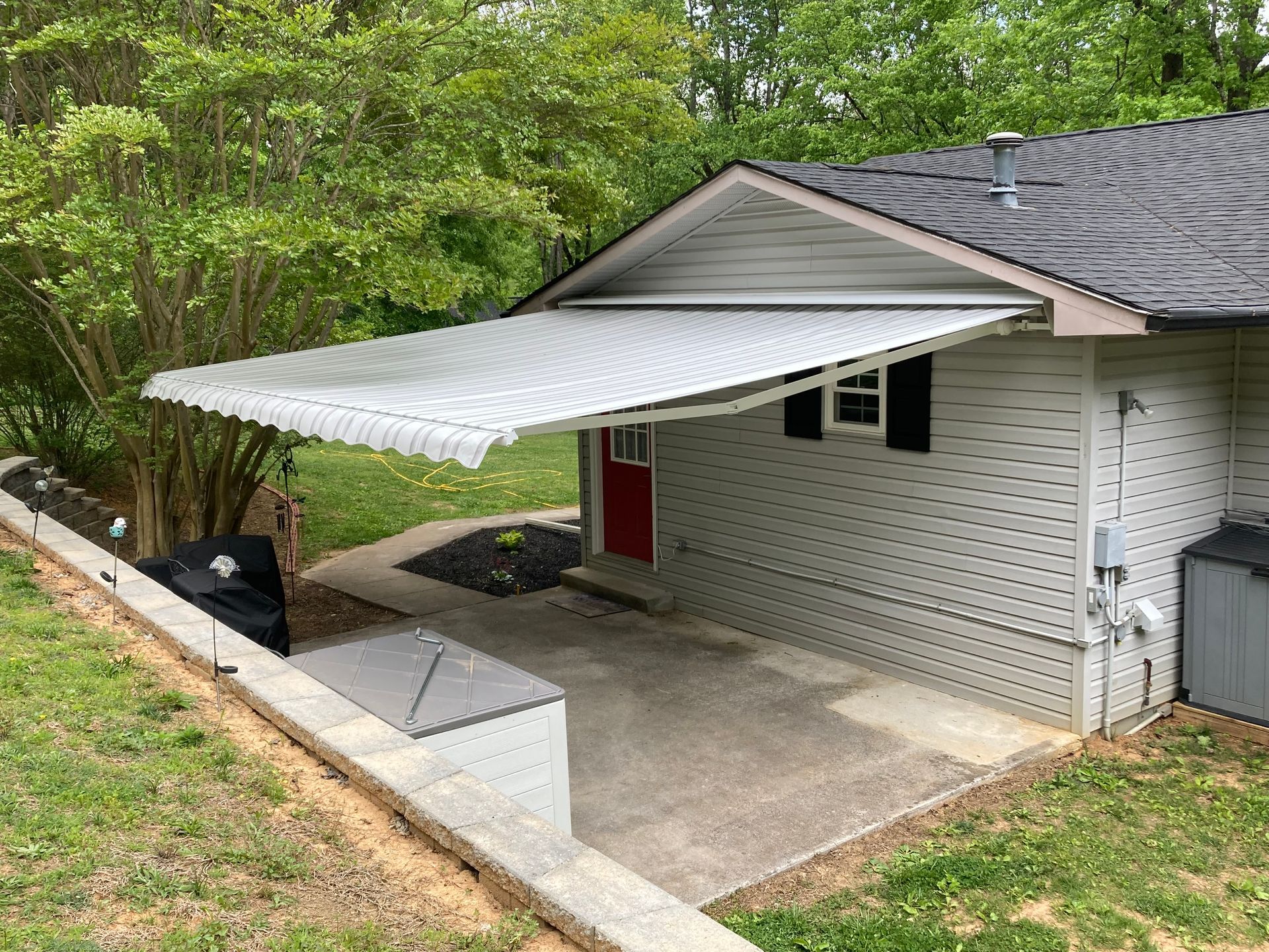 White retractable awning over a small building's patio with a red door.