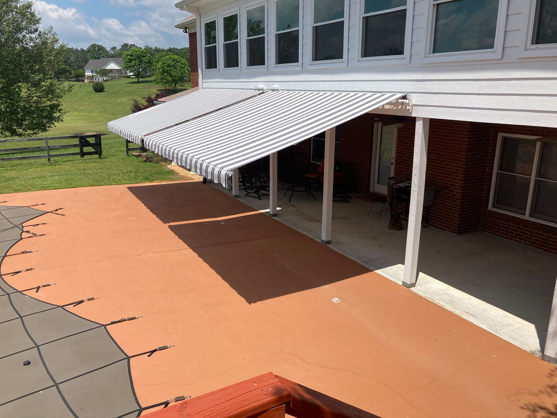 A house with white and black striped awnings extending over a wooden deck with a pool.