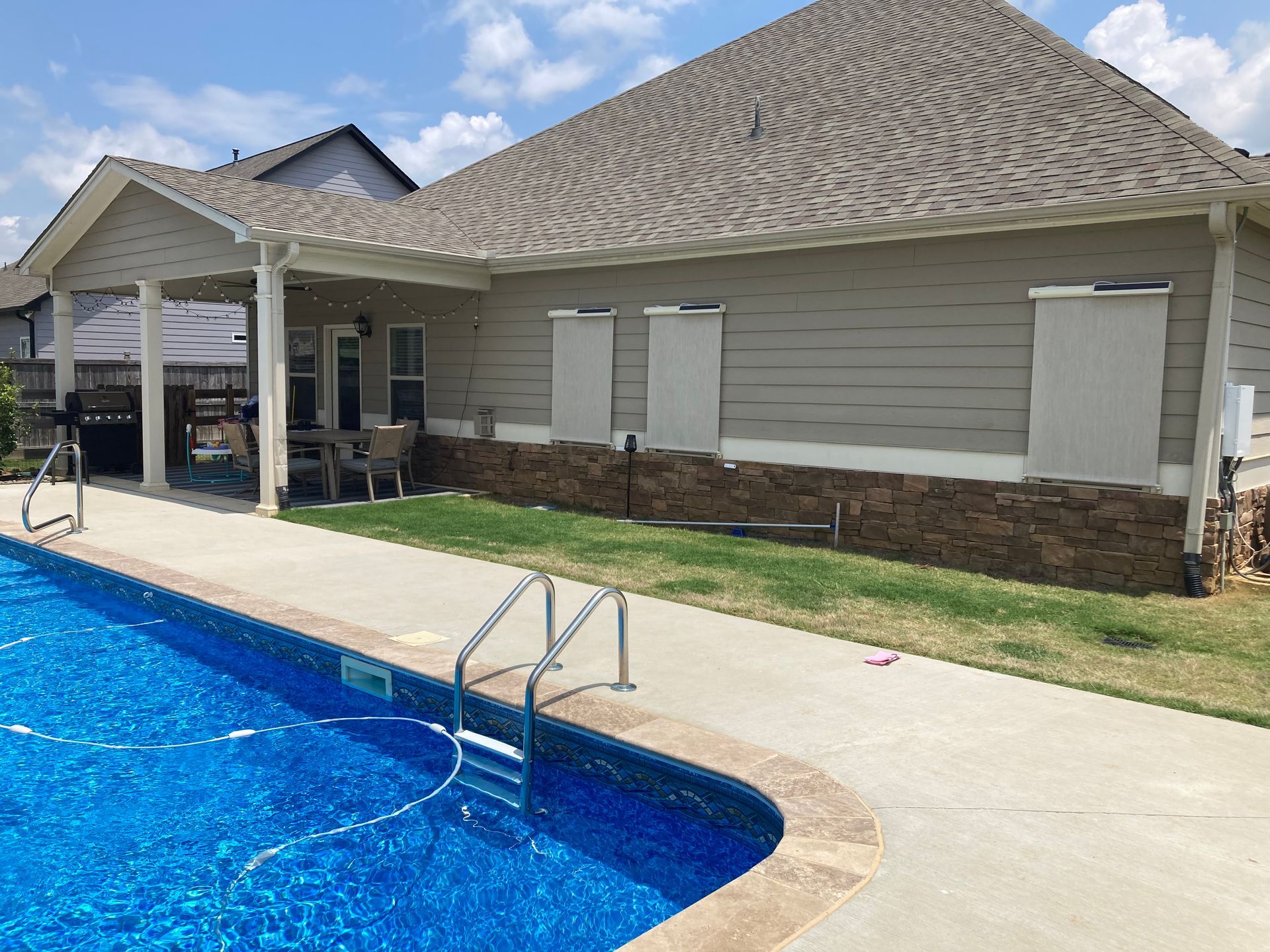 Swimming pool next to a house with outdoor porch and closed white shutters.