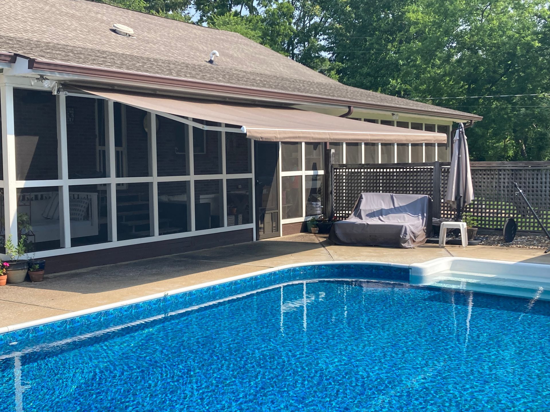 Brown retractable awning over a screened porch and swimming pool.