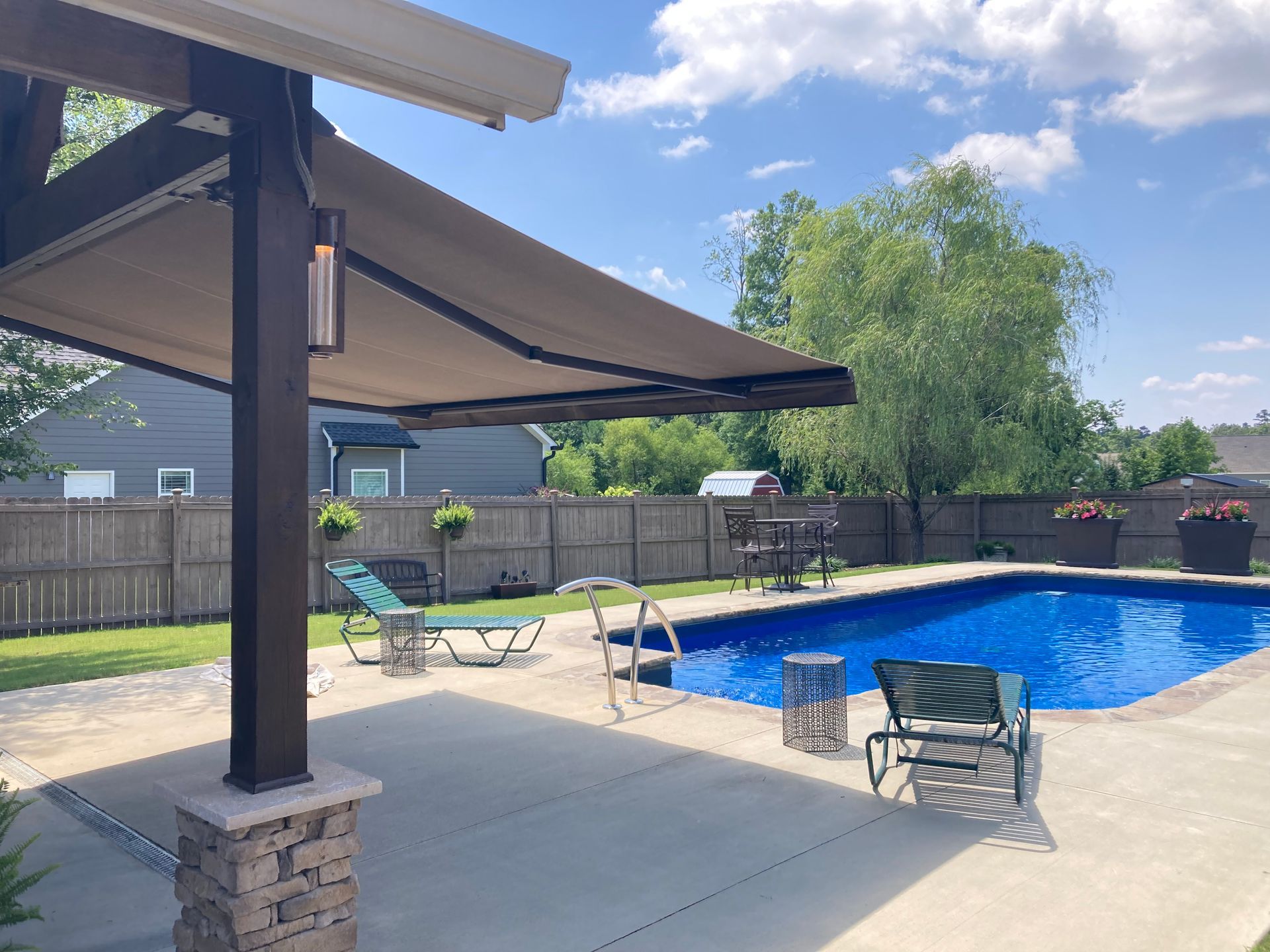 Patio with awning, pool, and lounge chairs on a sunny day.