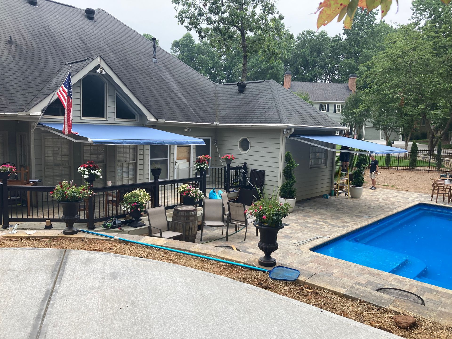 Backyard with a pool, deck, awnings, and an American flag.