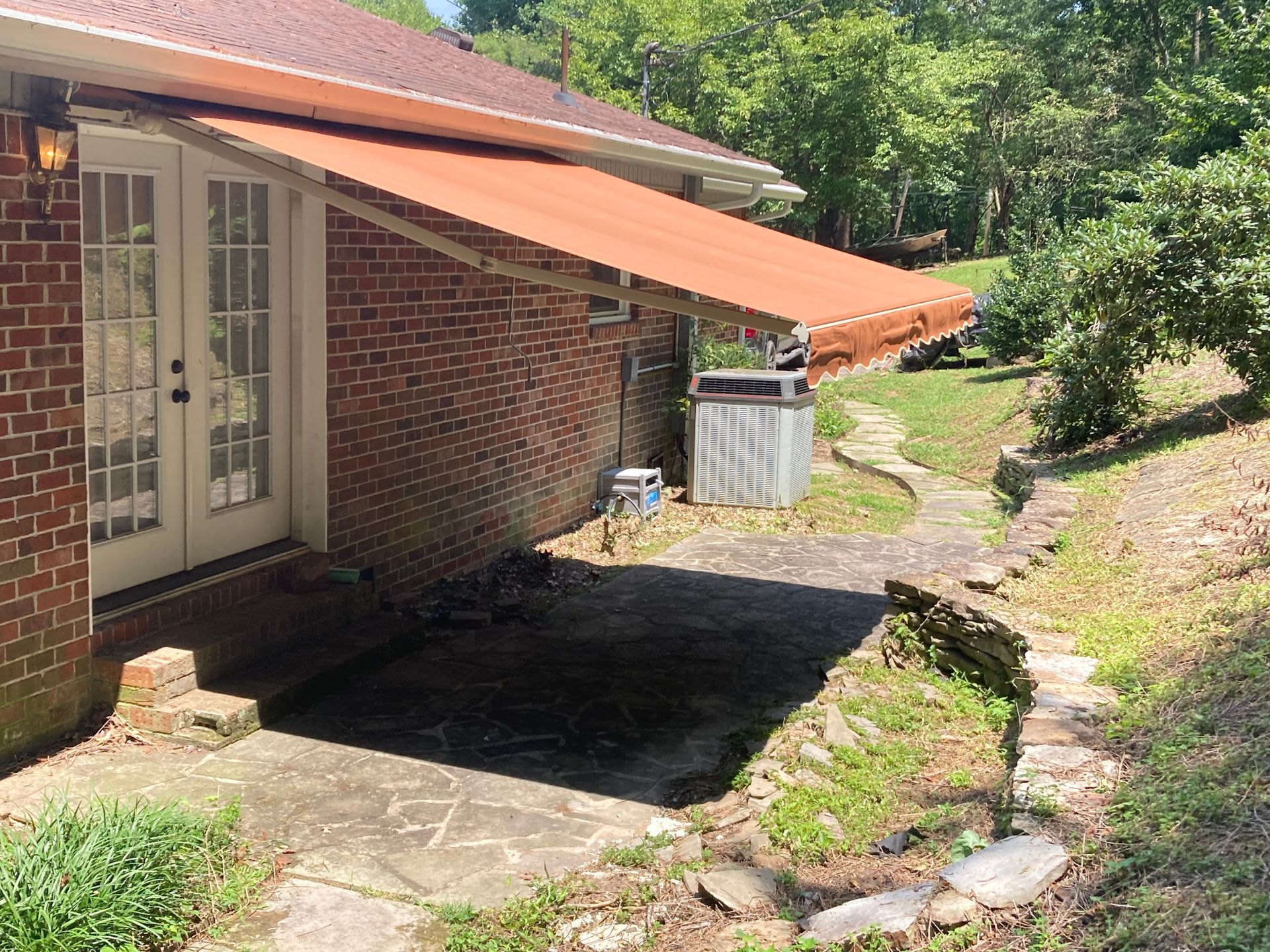 Brick building with orange awning over a concrete patio. Stone steps lead up a grassy hill.