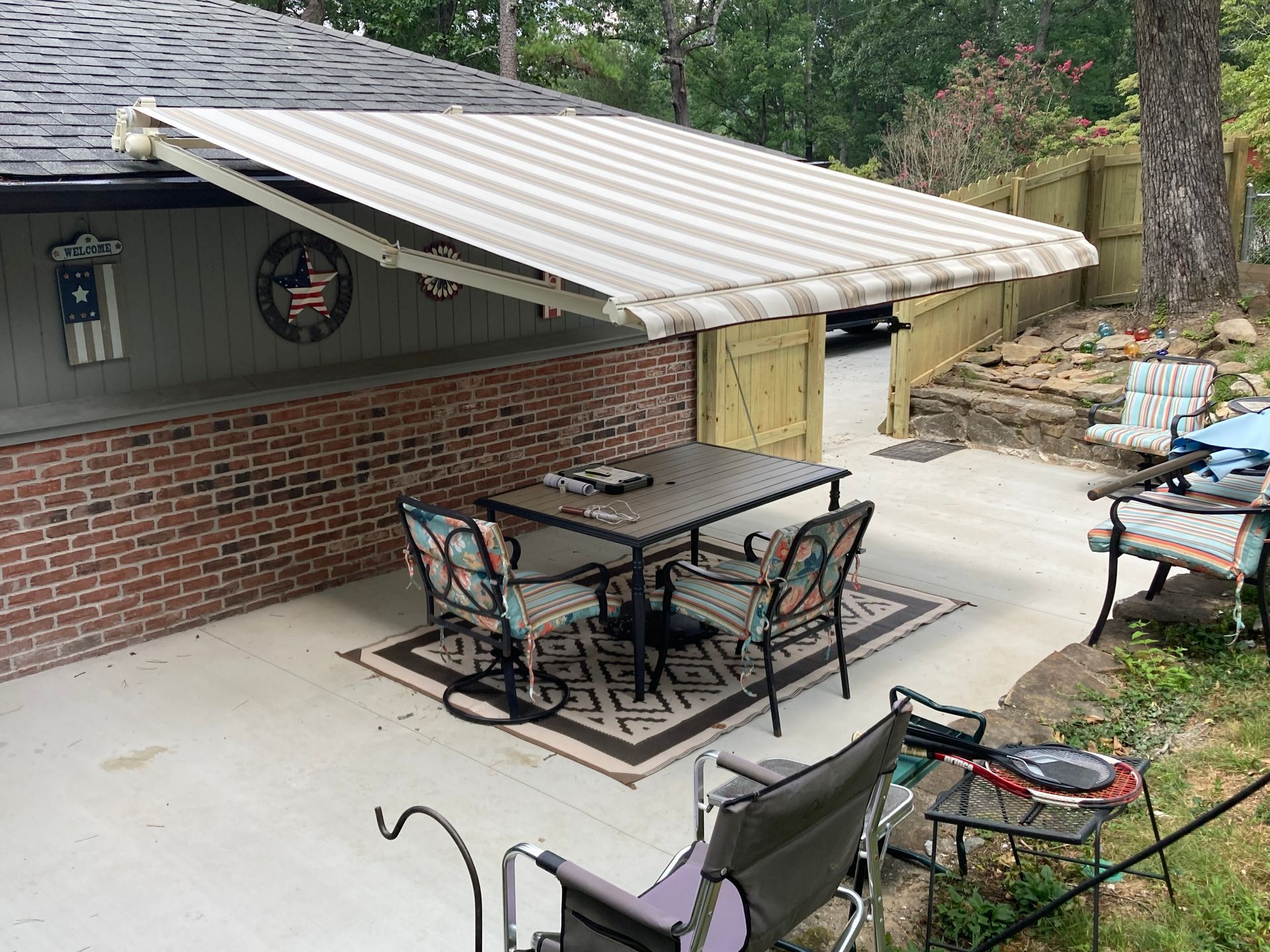 Patio with retractable striped awning over a table and chairs on a concrete patio.