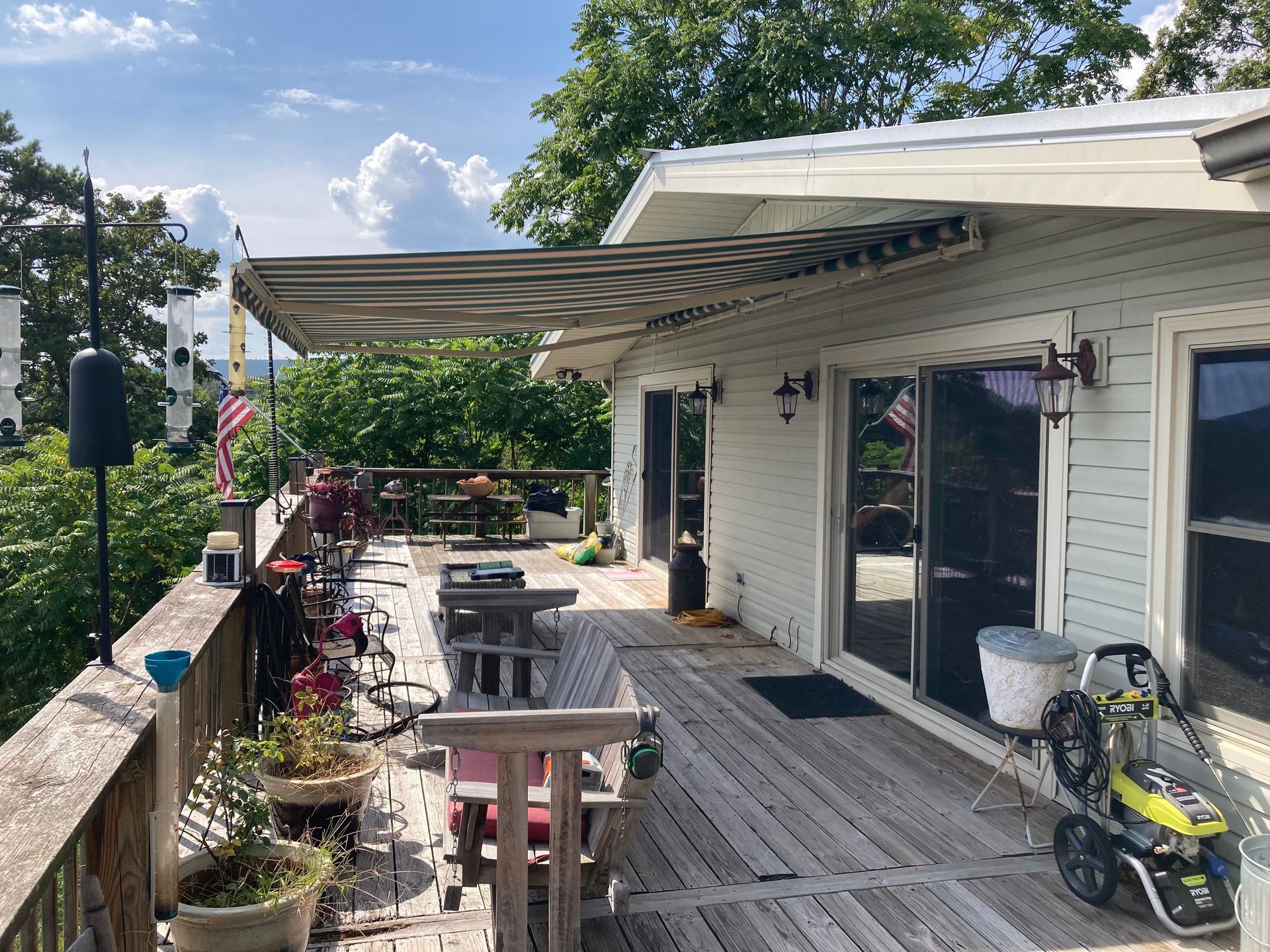 Wooden deck with awning over glass doors; potted plants, table, and pressure washer visible.