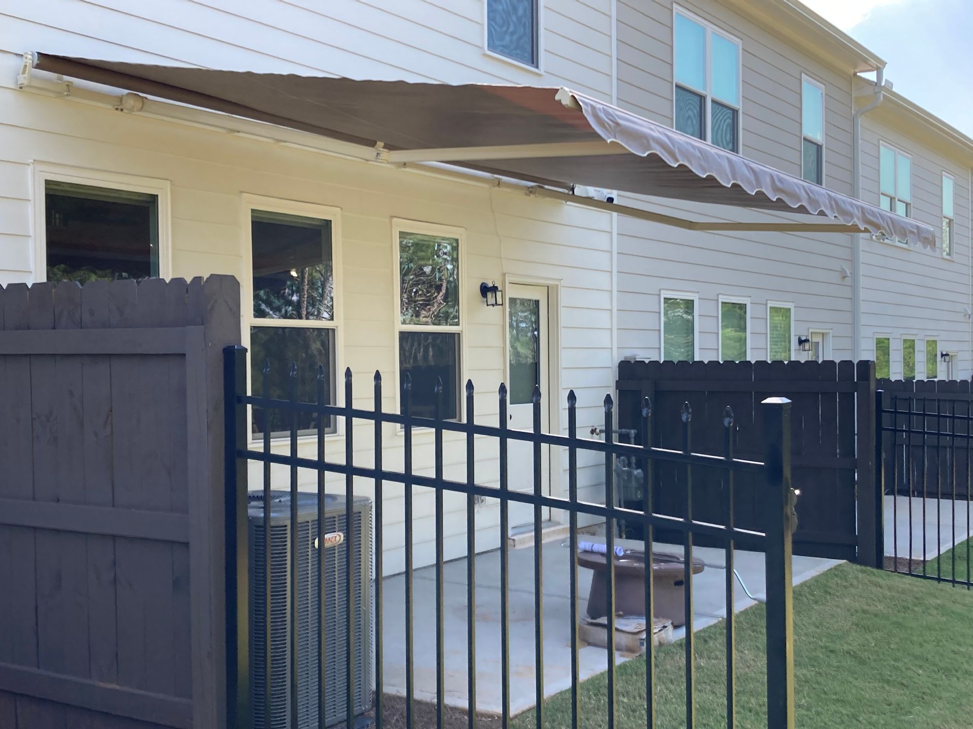 Exterior of a beige building with a brown awning, black fence, and small patio.