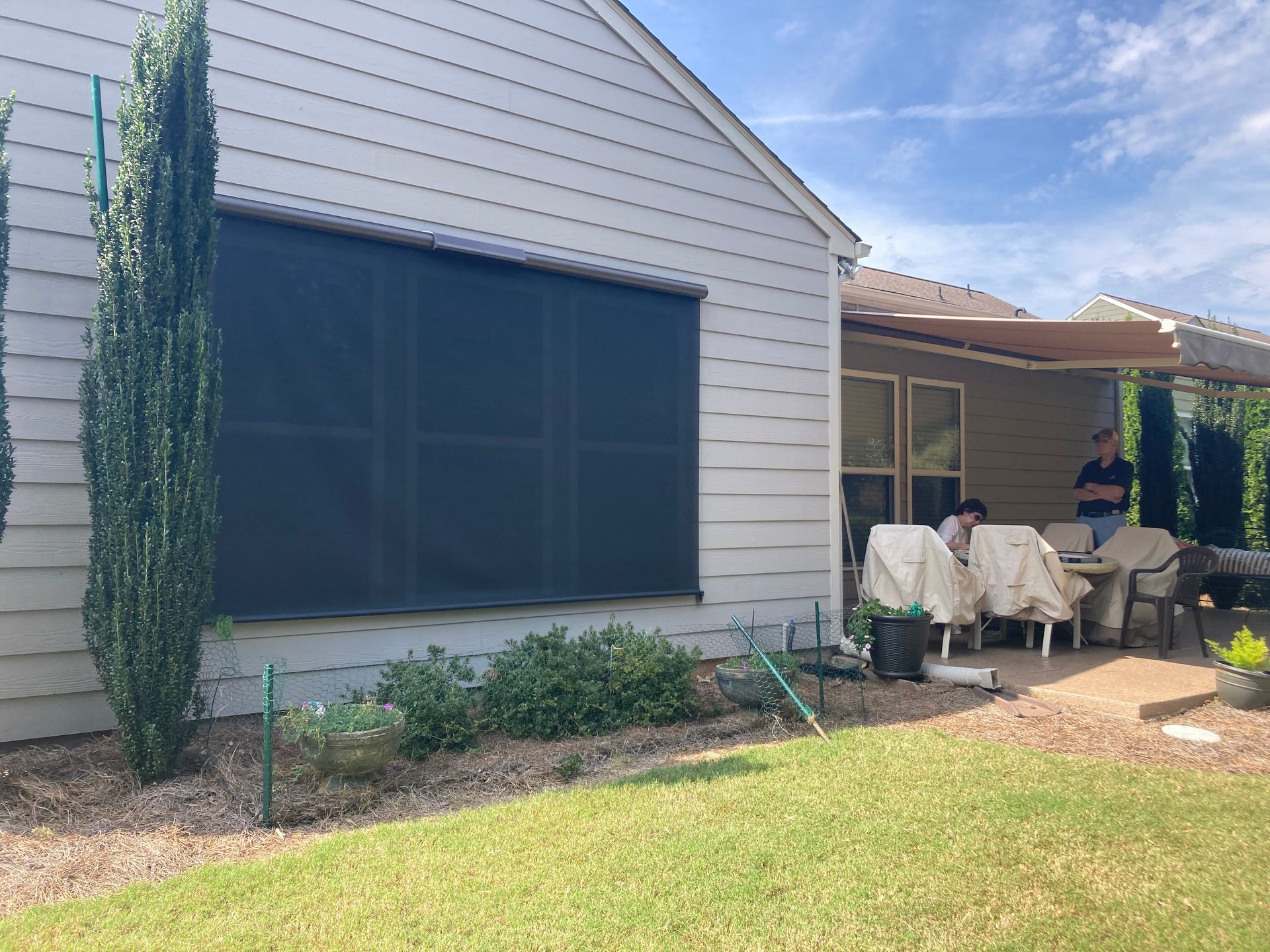 Exterior of a house with a large black screen and a patio with people and furniture.
