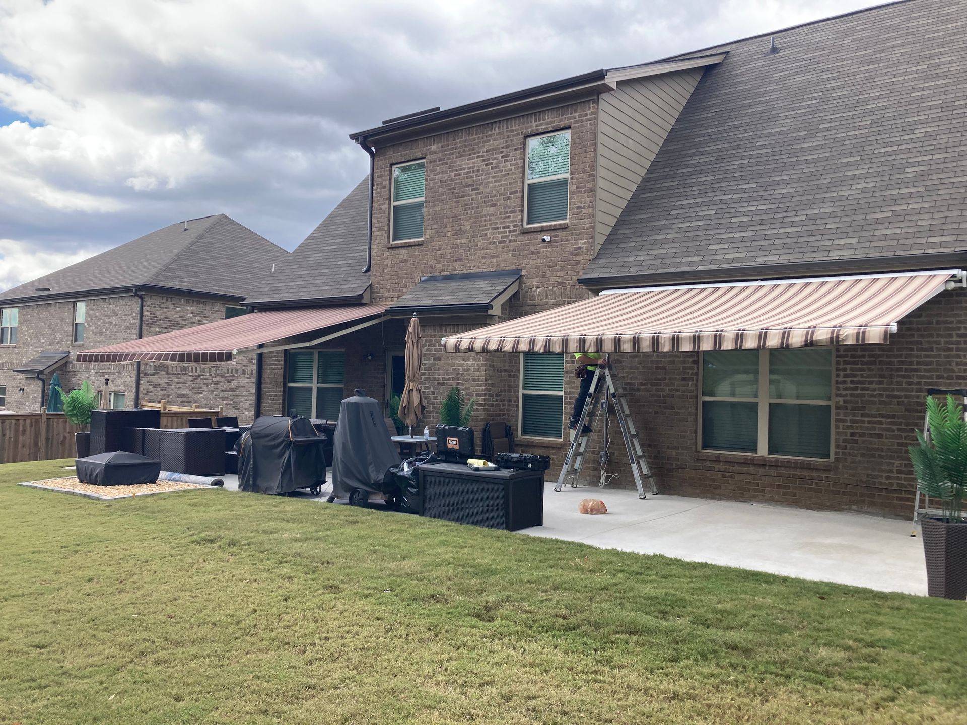 Backyard with two awnings over patio, brick houses, and grassy lawn.
